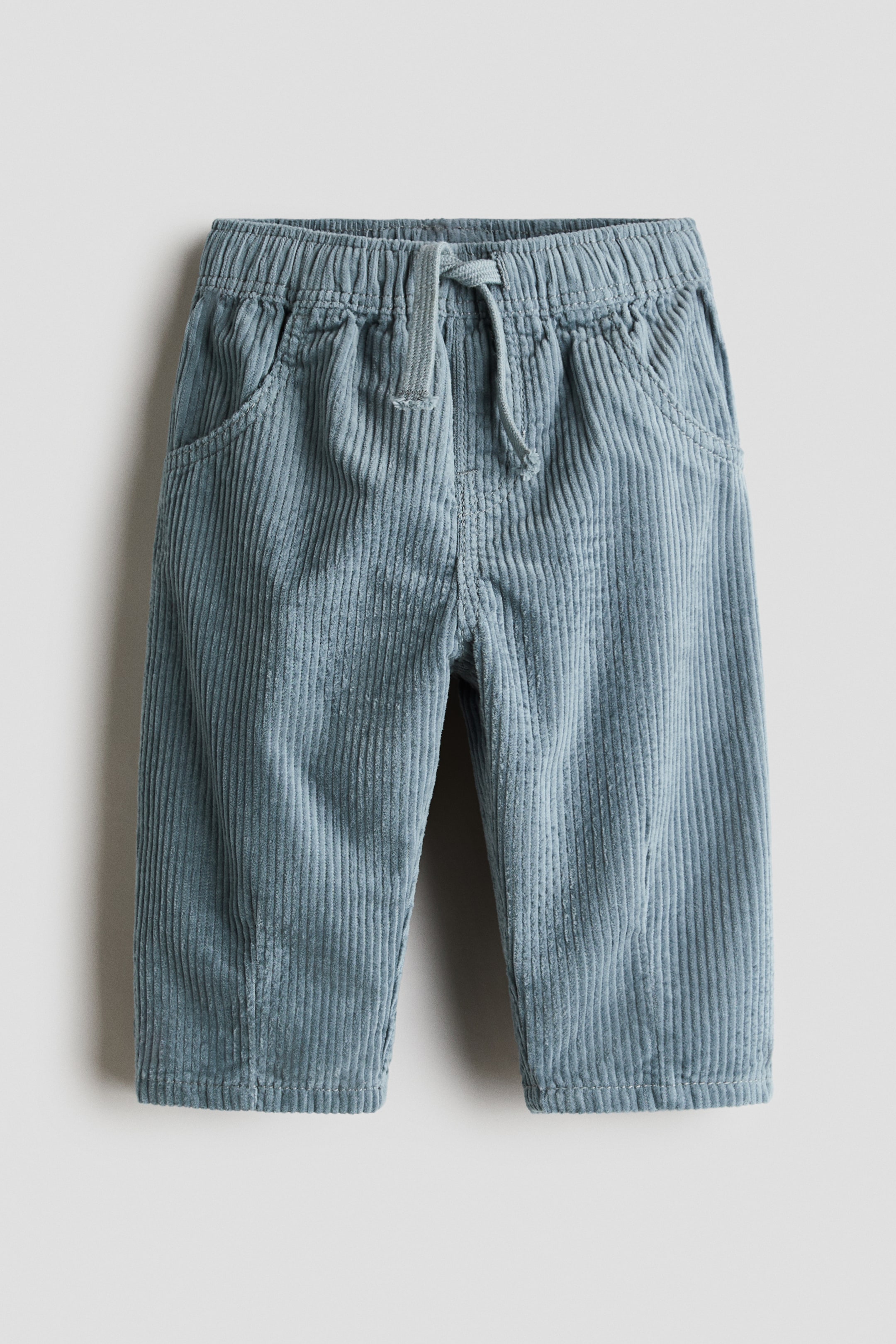 Agrandir l'image: Un jogging en velours côtelé de coton bleu poudré est présenté de face, avec une taille élastiquée à cordon de serrage et une braguette factice. Le pantalon présente des poches avant décoratives incurvées et une coupe droite avec une texture côtelée verticale.