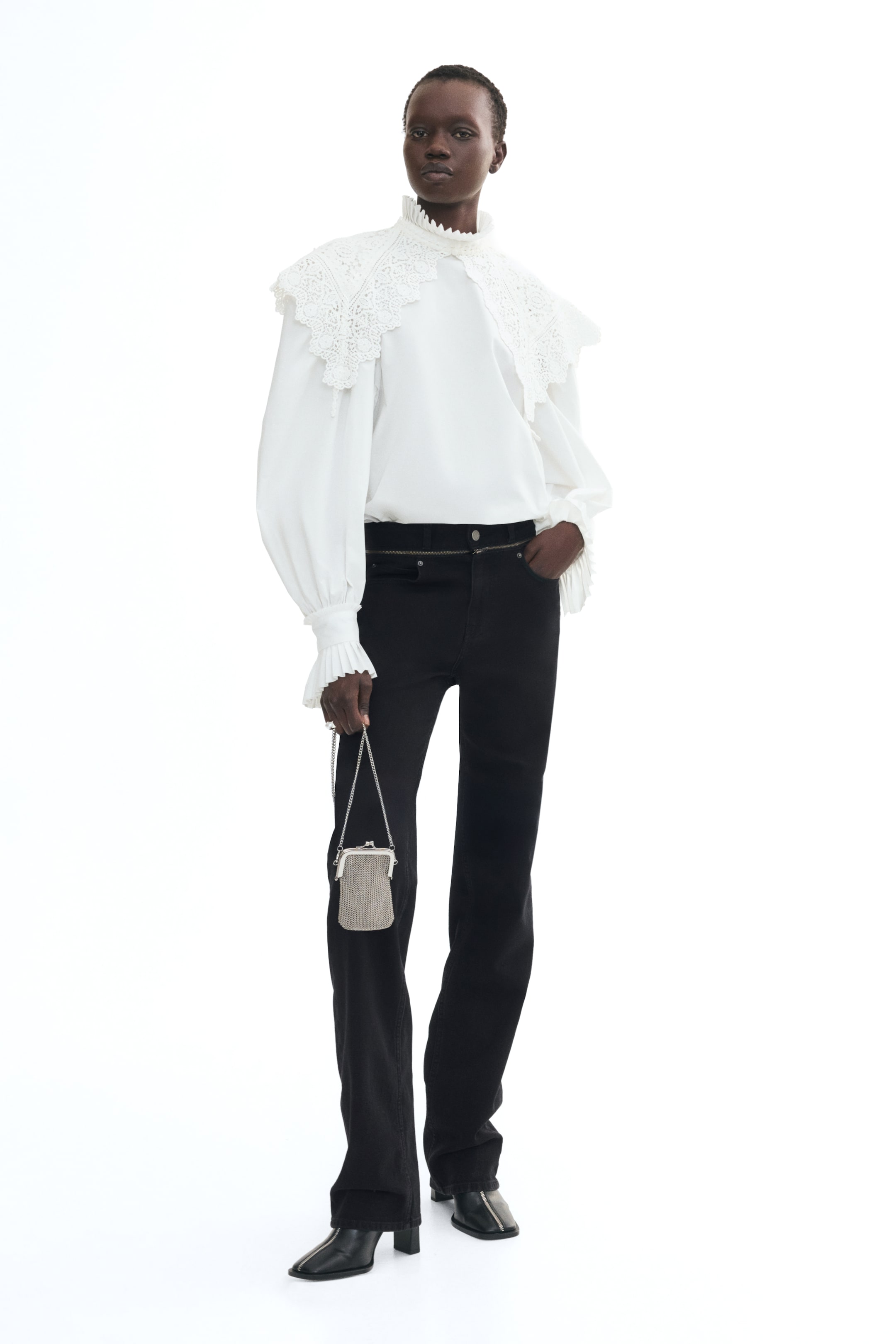 View larger image: Black five-pocket jeans with a regular waist and straight legs are worn by the model, who is standing with one hand resting in a front pocket. The jeans are styled with a white blouse with a high collar and large lace detailing, paired with black heeled boots.