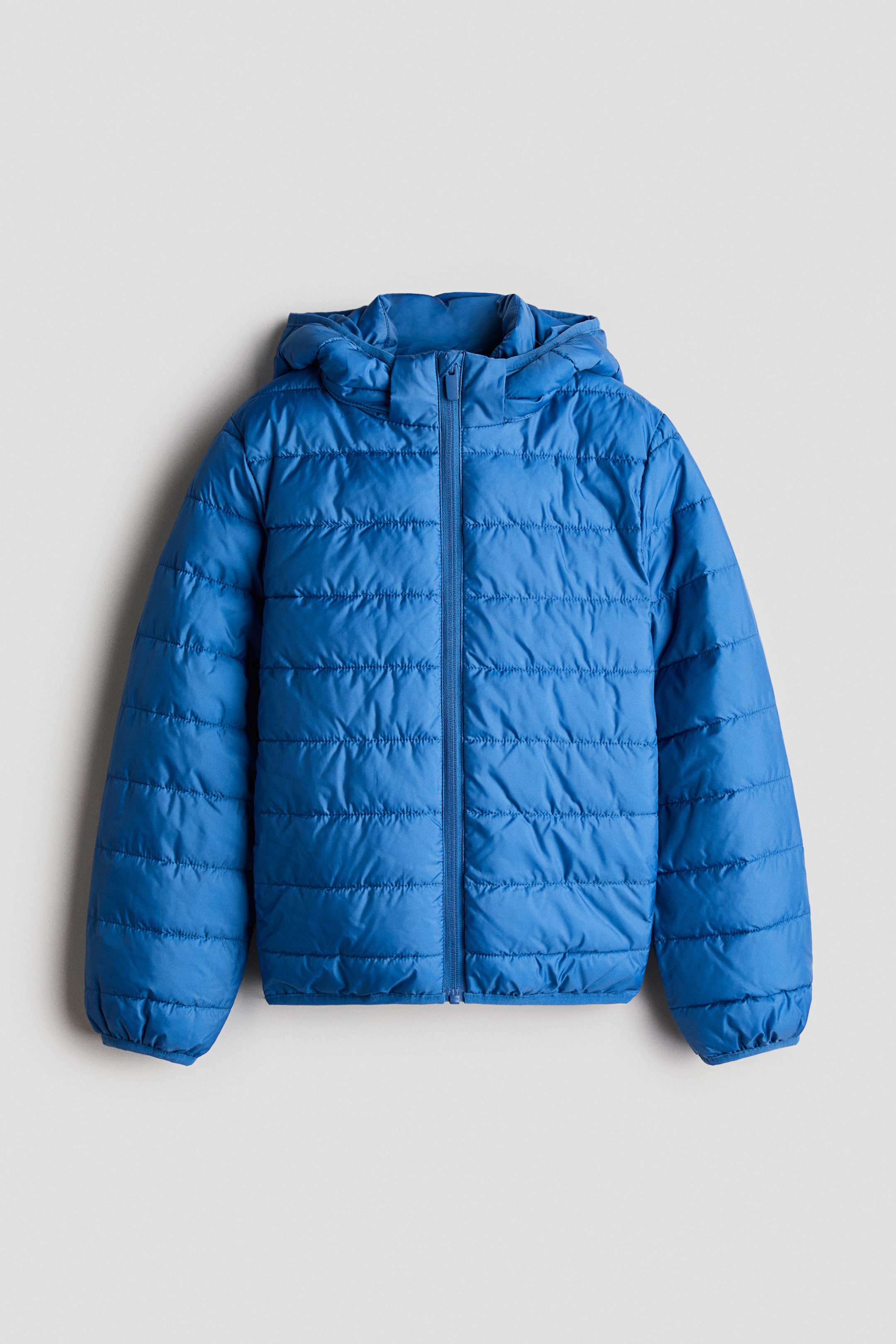Voir une image plus grande: Une veste matelassée bleu avec capuchon est vue de face, présentant des surpiqûres horizontales et une fermeture à glissière intégrale. La veste comprend un capuchon attaché, des manches longues avec poignets élastiques et un ourlet droit.