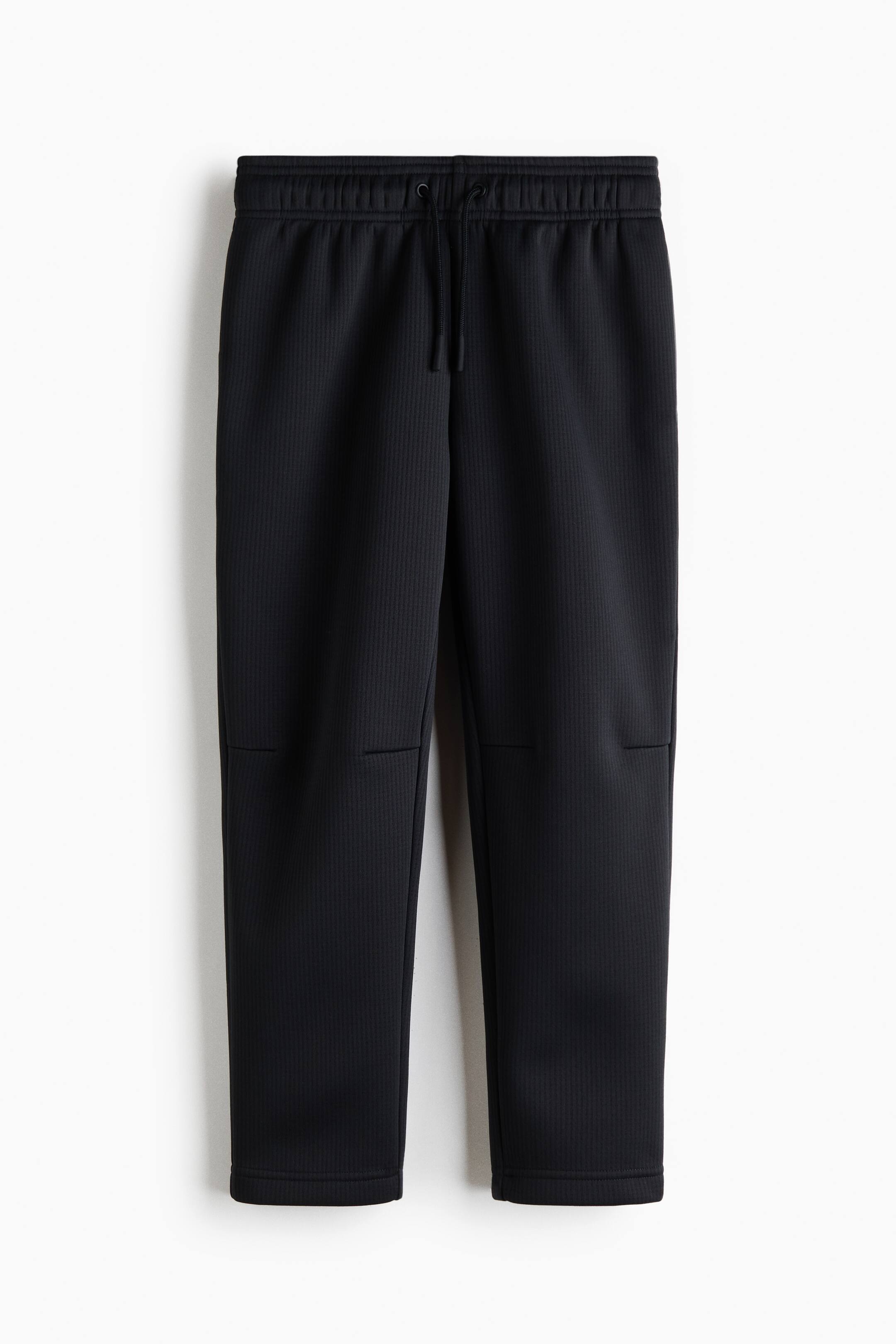 View larger image: These black textured sweatpants are shown front-facing, featuring an elasticated ribbed waistband with an adjustable drawstring. The fabric displays a subtle vertical ribbed texture with horizontal seam details across the knees and straight-cut hems.