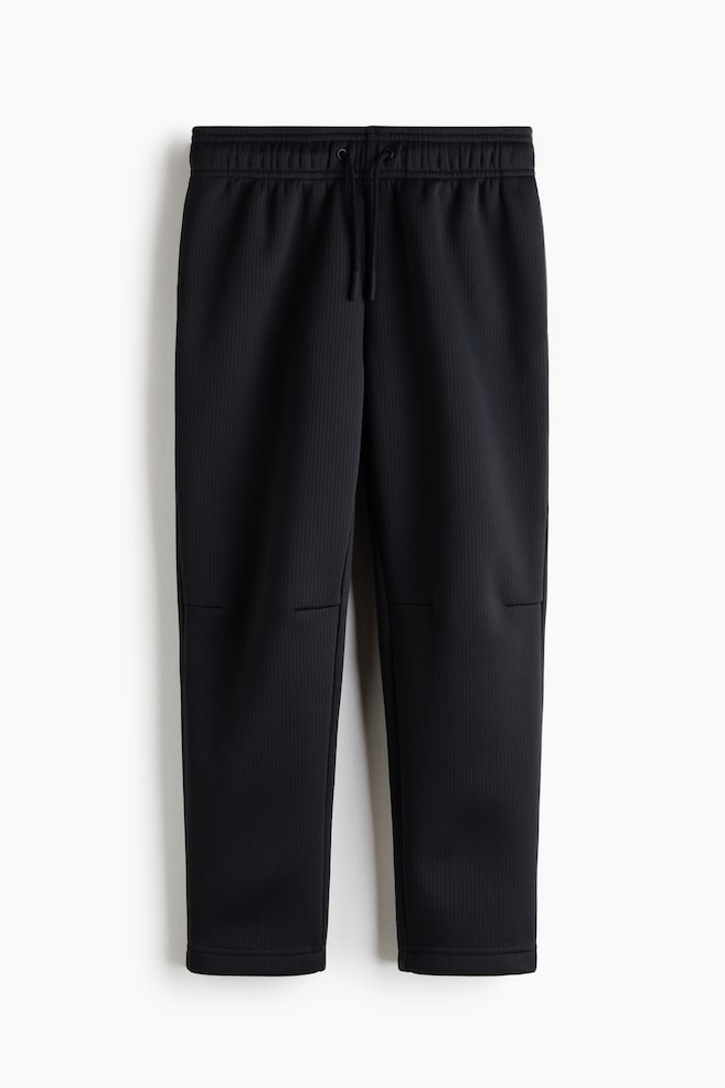 These black textured sweatpants are facing front, featuring an elasticated ribbed waistband with an adjustable drawstring. The fabric is displaying a subtle, vertical ribbed texture with horizontal seam details across the knees and straight-cut hems. - 1