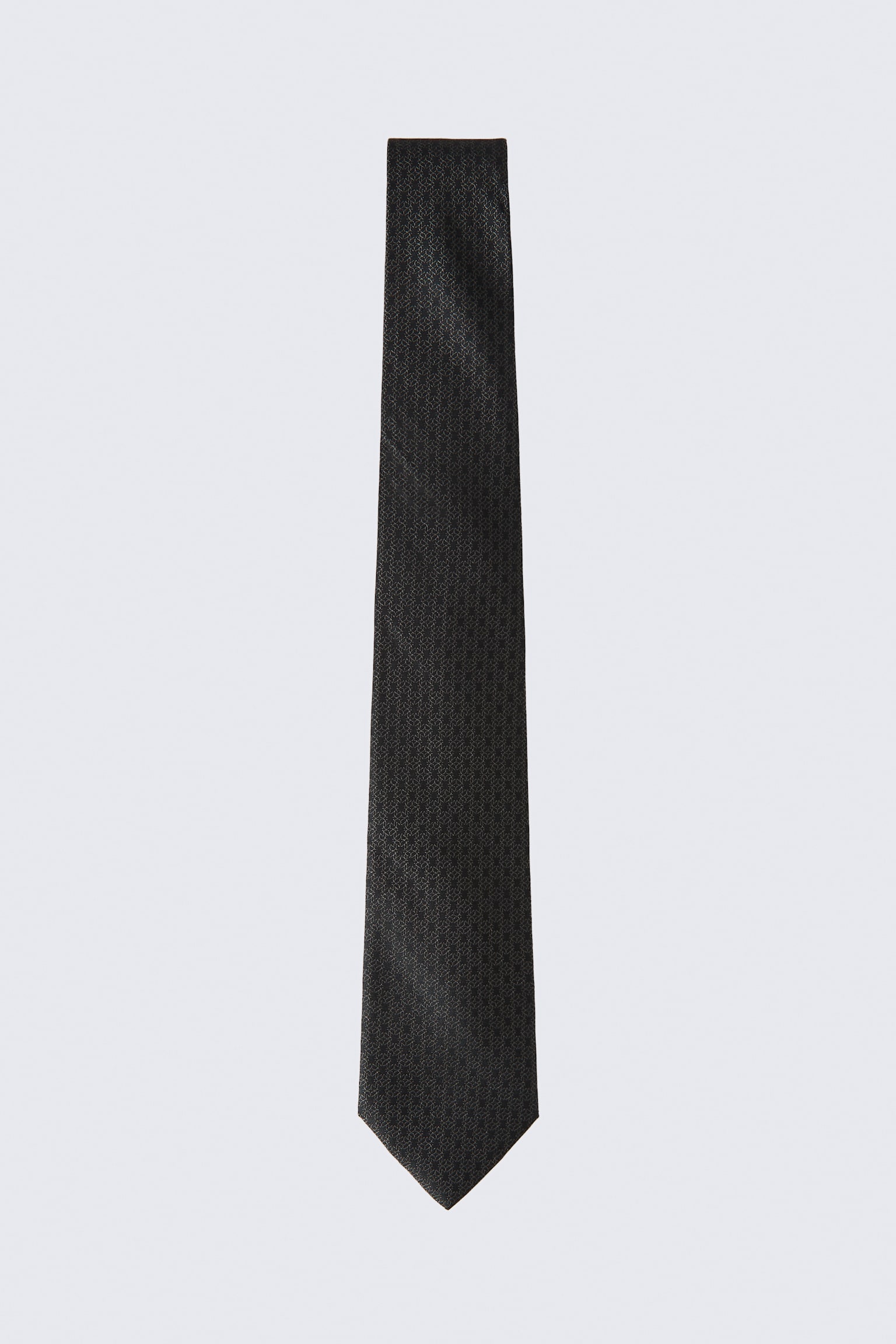 Una corbata de seda con tejido jacquard en gris oscuro cuelga de forma vertical, mostrando un sutil patrón geométrico jacquard repetido a lo largo de toda su extensión. La corbata se ensancha ligeramente hacia la parte inferior y termina en una punta clásica.