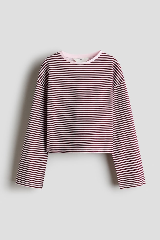 A long-sleeved top is shown from the front, featuring horizontal burgundy and light pink stripes. The top is designed with a solid pink, rib-trimmed round neckline, dropped shoulders, and long, wide sleeves. - 1