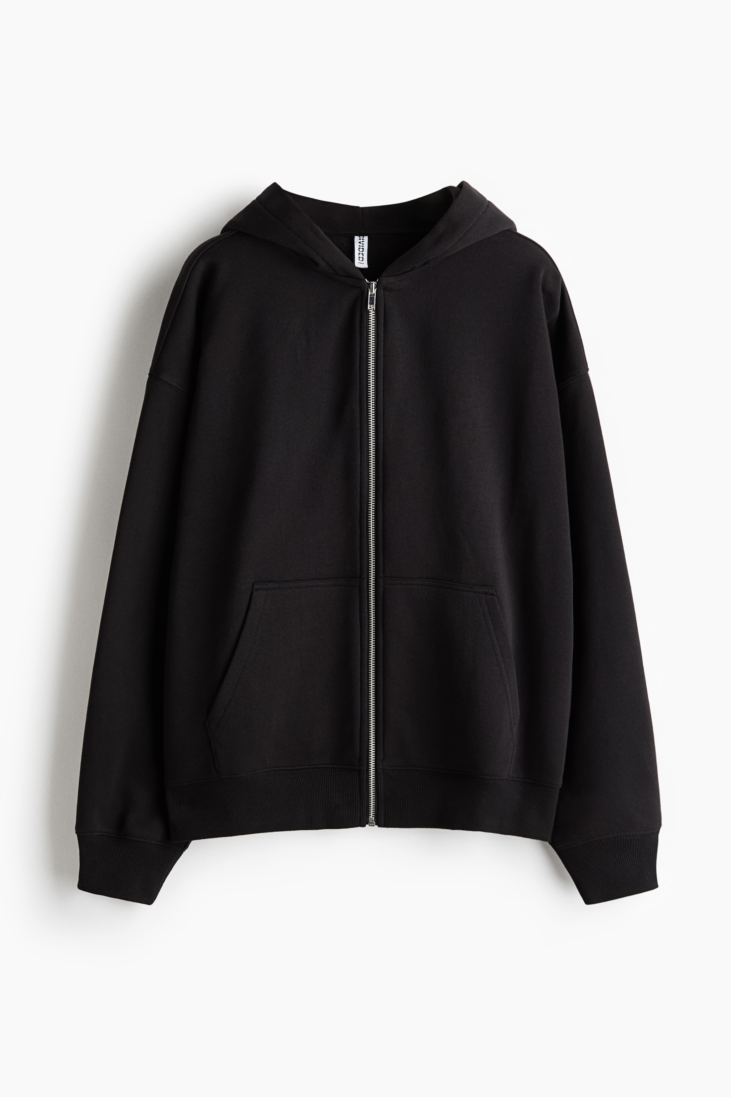 A dark brown zip-up hoodie in brushed fleece is worn open by the model, who has their hands resting in the front pockets. The hoodie features dropped shoulders, ribbed cuffs, and a hood, and is layered over a black crop top and paired with wide-leg denim shorts.