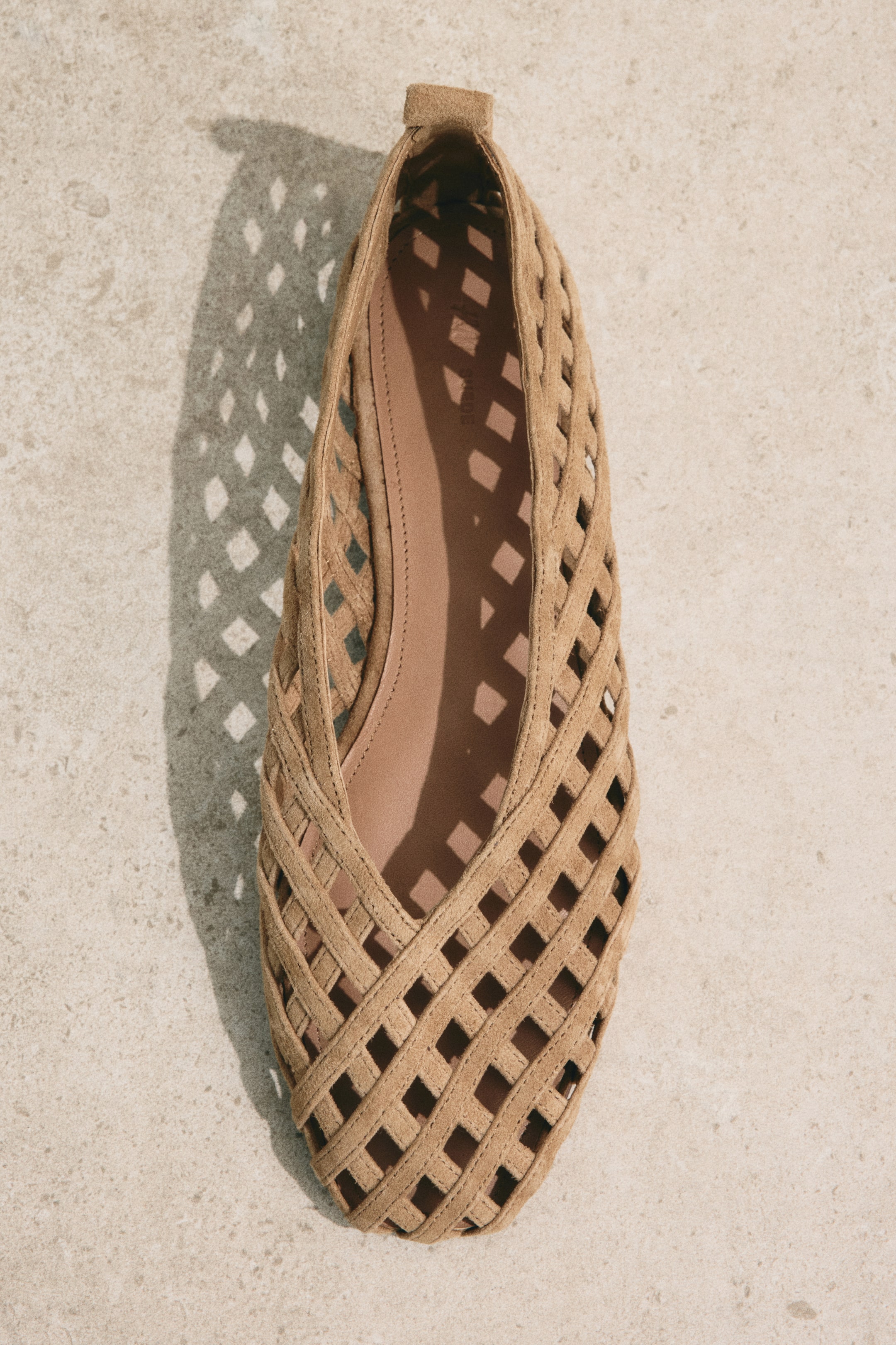Zobacz większy obraz: Płaski but z jasnobrązowego zamszu prezentuje plecioną cholewkę z kwadratowymi wycięciami. Wewnątrz widoczna jest jasnobrązowa wkładka, a but jest skierowany do przodu z perspektywy z góry.