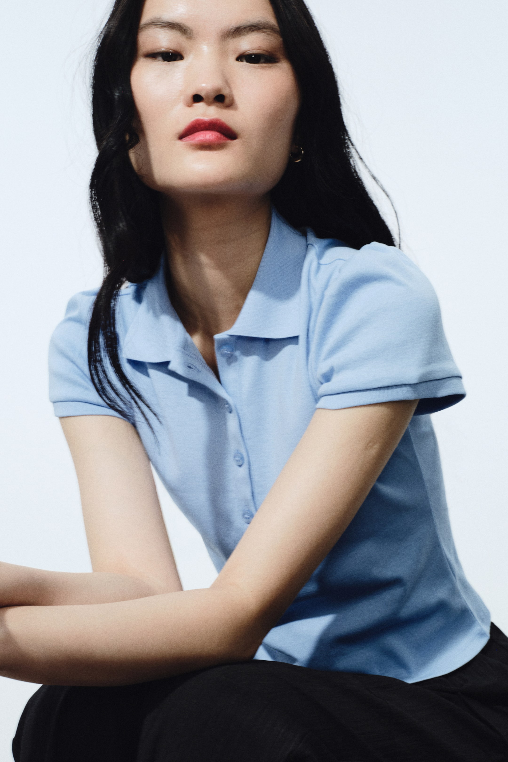 拡大画像を表示: ライトブルーのニットポロシャツは、クラシックなポロカラーと同系色のボタンを配した前立てを備えています。ショートスリーブはきれいな裾仕上げで、上半身に沿うフィット感です。