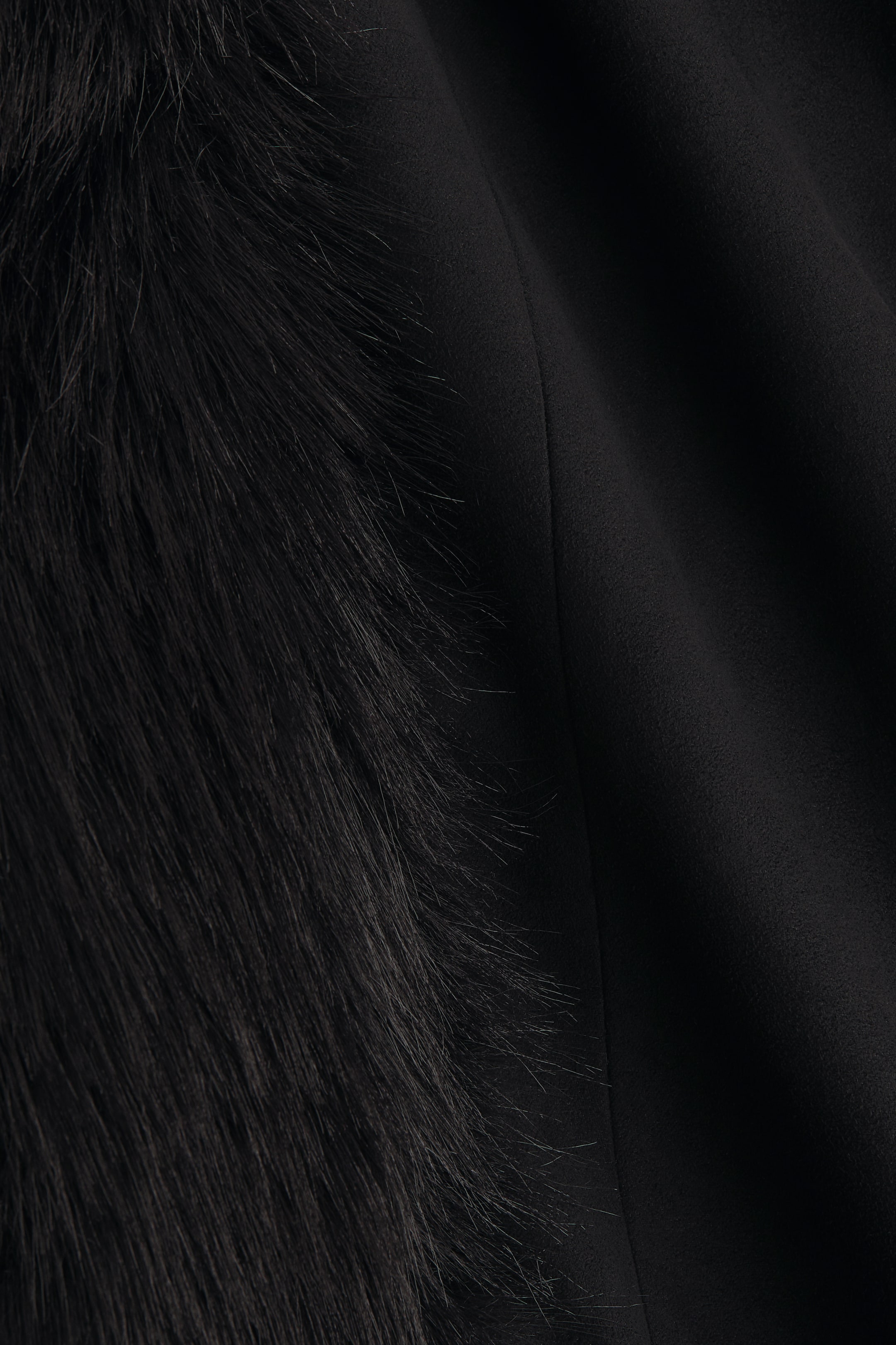 Agrandir l'image: Le produit présente un gros plan de deux textures noires contrastées : une fausse fourrure longue et sombre à gauche, et un tissu lisse et mat à droite, séparés par une couture verticale distincte.