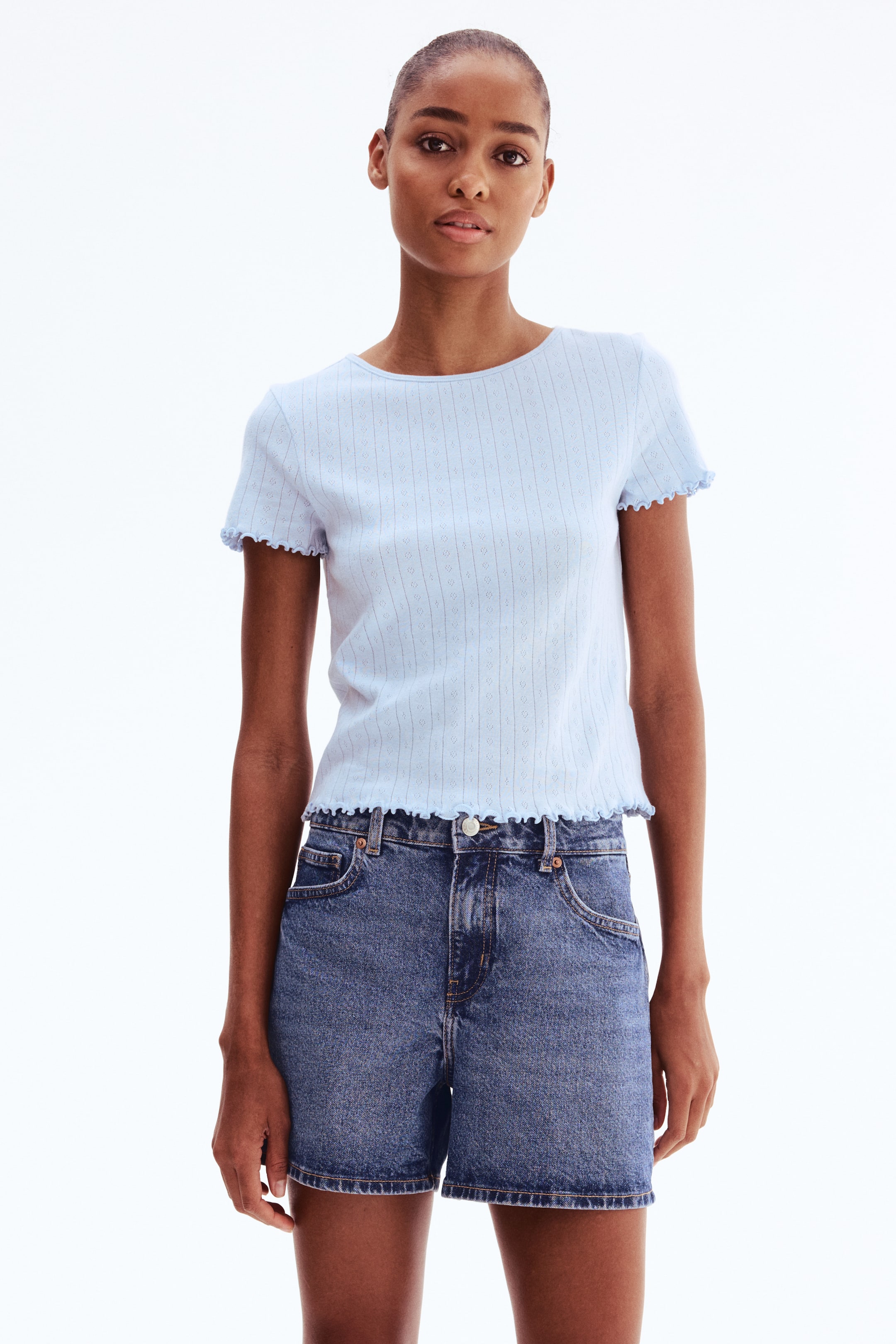 View larger image: The model wears a light blue top in soft pointelle jersey, featuring a round neckline and short sleeves. Overlocked edges are visible at the cuffs and hem.