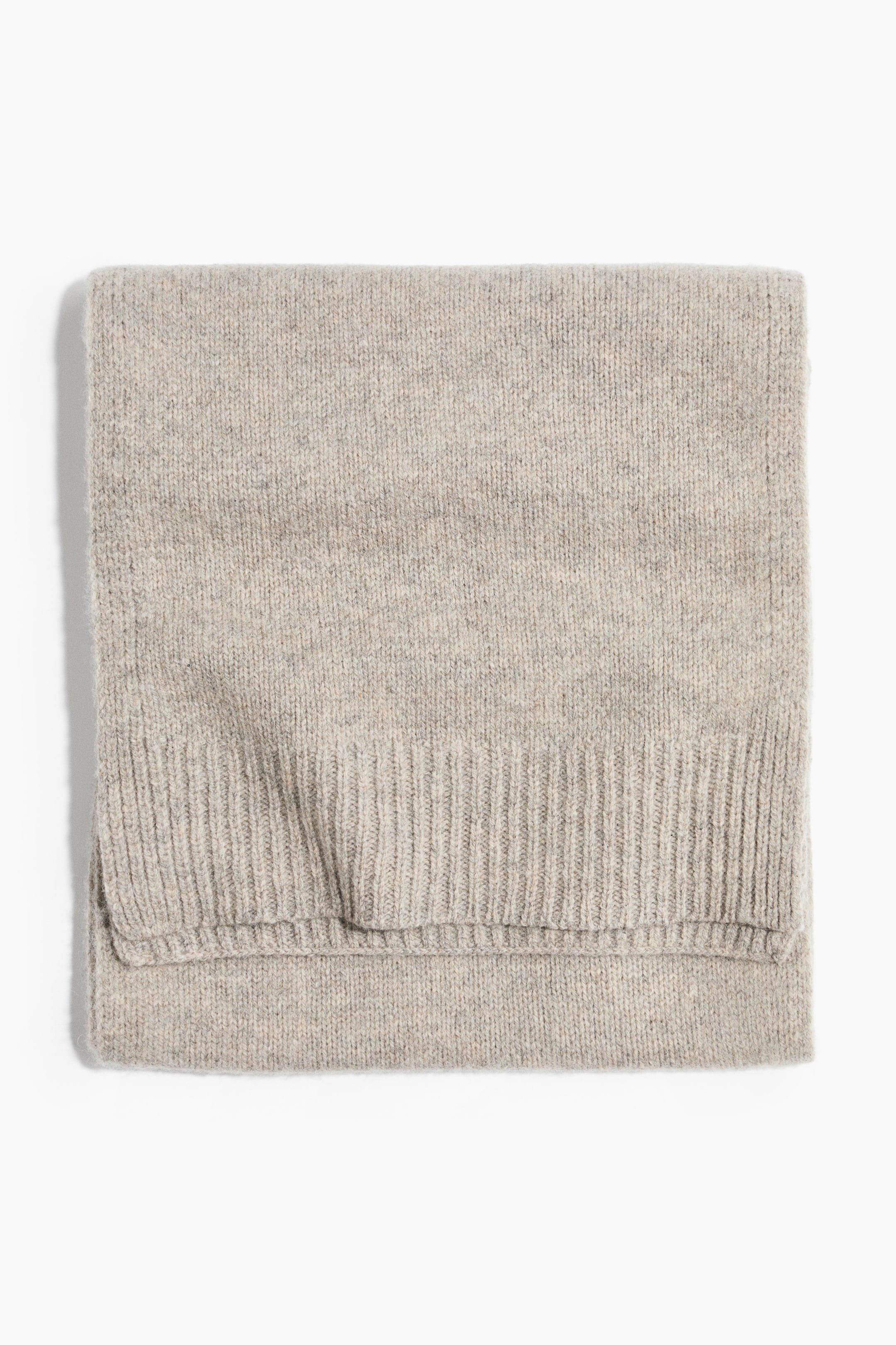 Größeres Bild ansehen: Ein hellbeiger Strickschal liegt flach zusammengefaltet und zeigt seine weiche, fein gestrickte Textur sowie eine breite Rippenkante am Rand.
