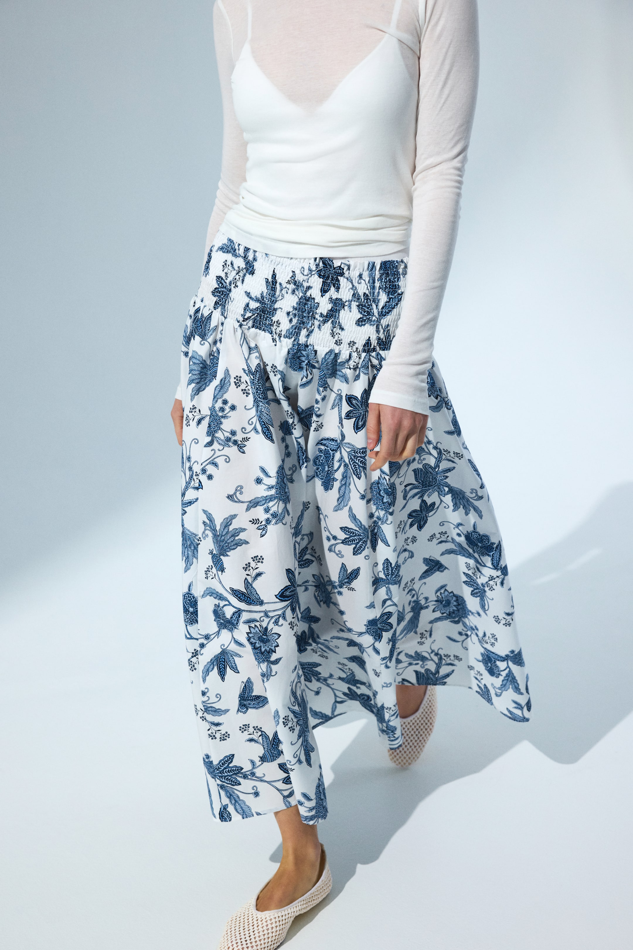 View larger image: White wide-leg pants feature a blue floral and botanical pattern, shown from a slight front-left angle. They are designed with a shirred elastic waistband, showcasing a flowy, full-length silhouette.