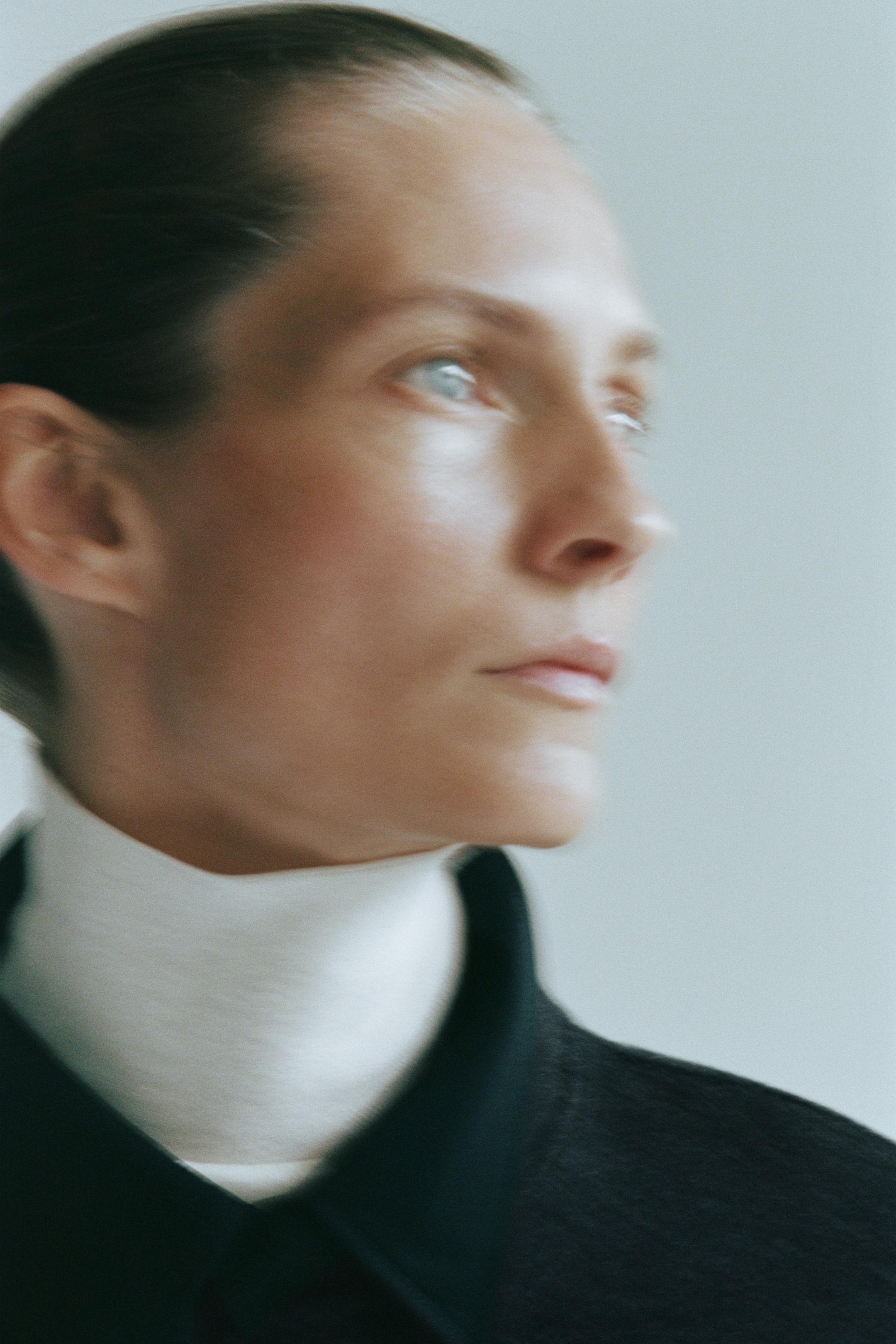 View larger image: A dark, brushed wool-blend jacket with a band collar is being worn by the model, layered over a high-neck white roll-neck top.