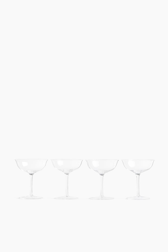 Four coupe glasses made of delicate glass are standing in a row facing forward, each showcasing a gently rounded bowl, a slightly flared rim, and a slender stem. - 1