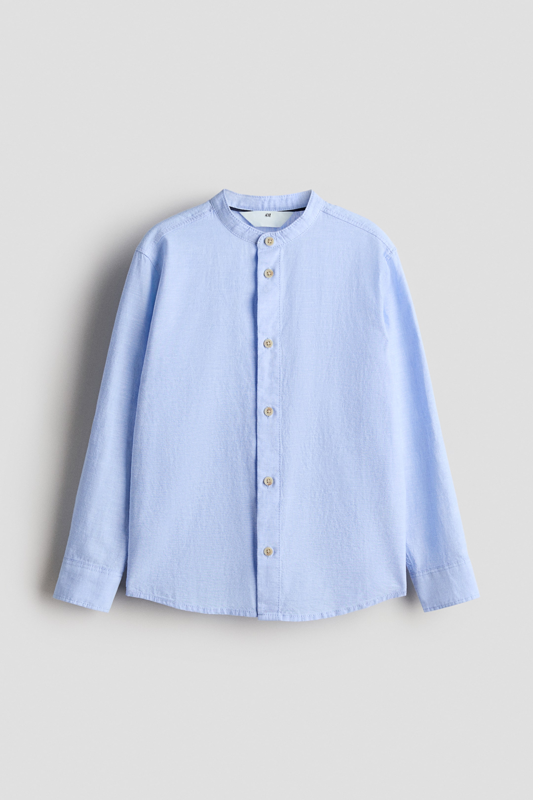 Agrandir l'image: Une chemise bleu clair est présentée de face (FRONT), dotée d'un col officier et de manches longues à poignets boutonnés. Des boutons marron clair habillent la patte de boutonnage sur toute sa longueur.