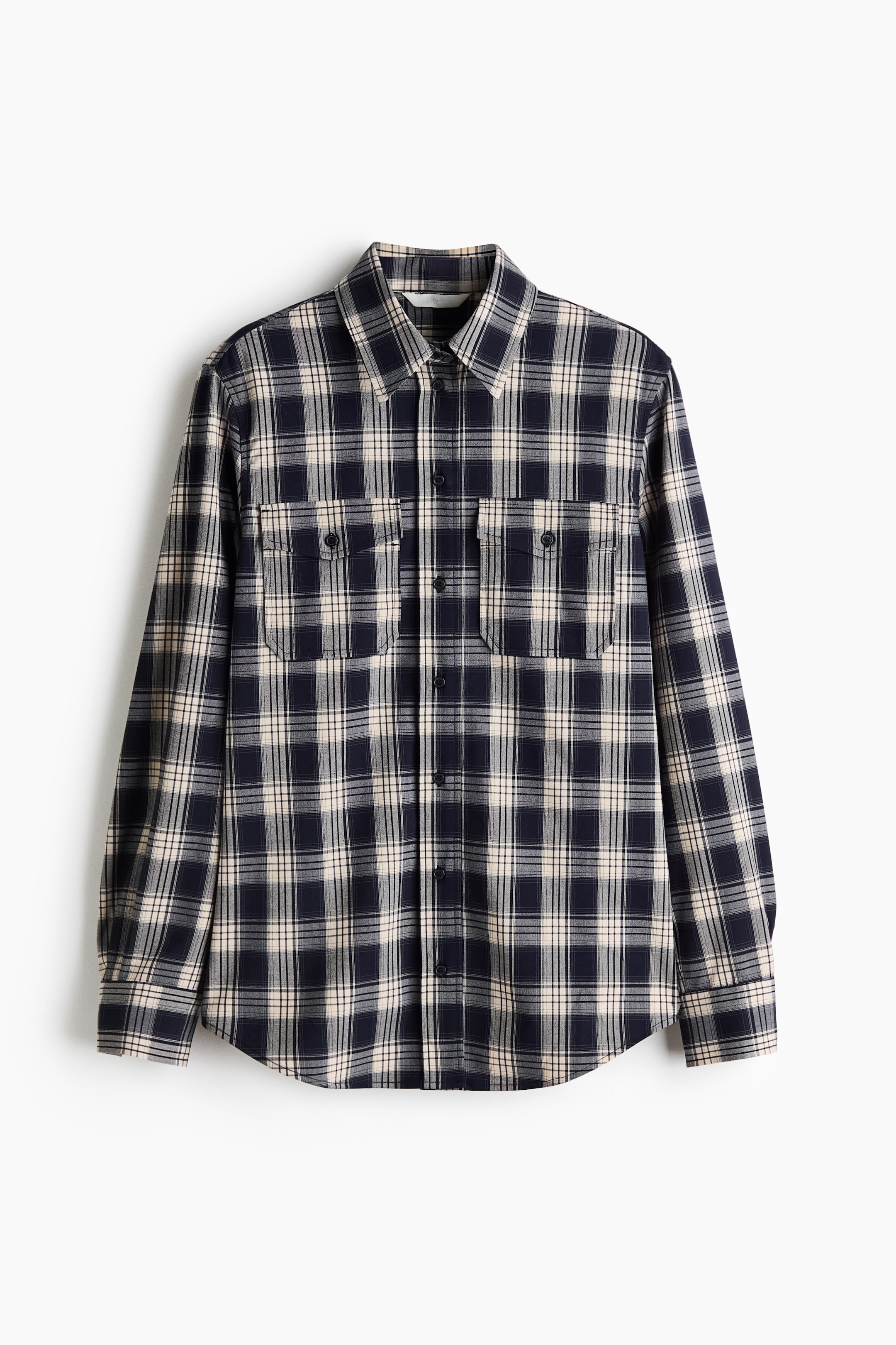 Ampliar la imagen: Una camisa de manga larga en tela tejida de cuadros muestra un patrón ajedrezado en azul marino y blanco roto visto de frente. La camisa presenta cuello, broches a presión al frente, dos bolsillos de parche con tapa en el pecho y cierre de broche a presión, y un dobladillo redondeado.