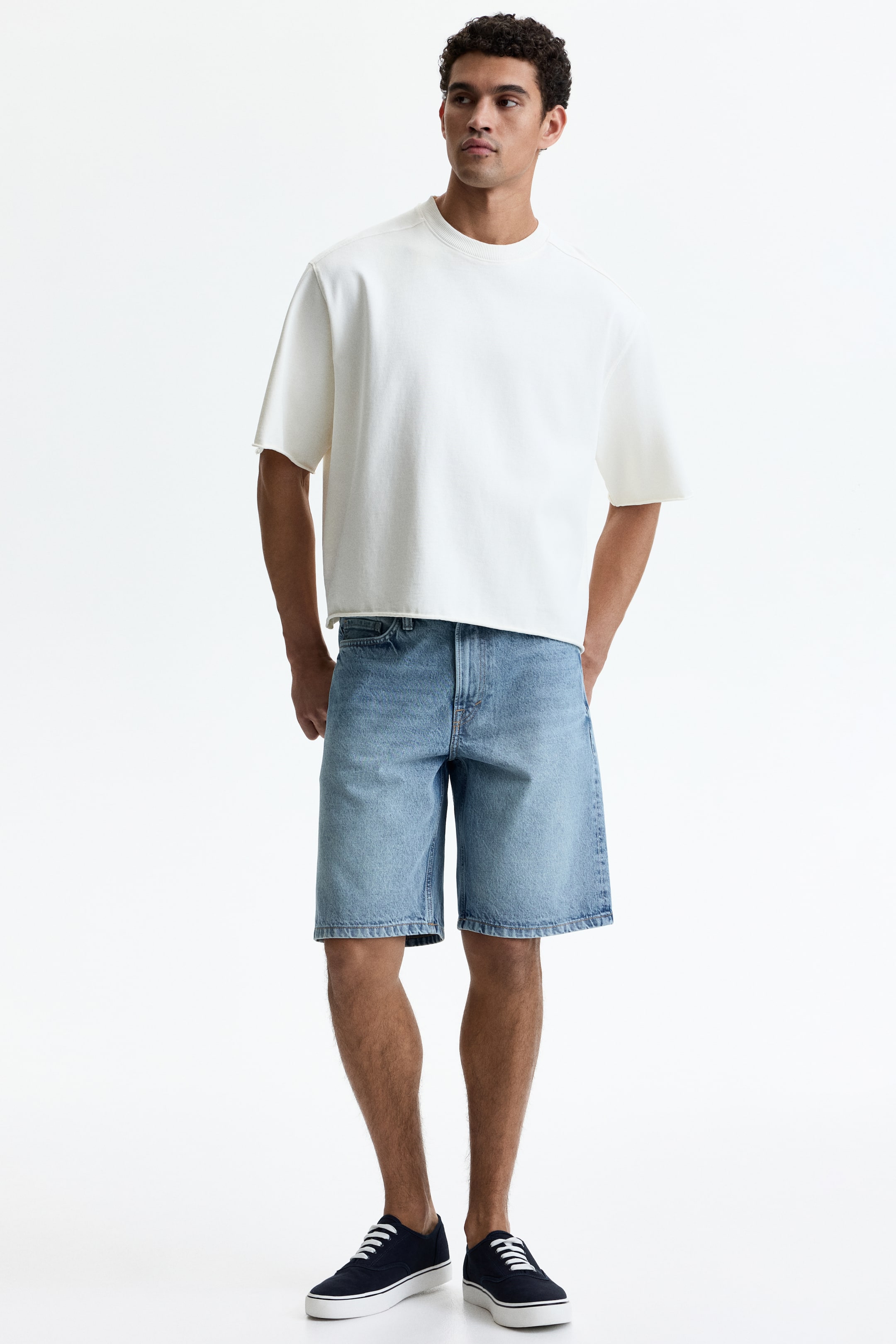 View larger image: A creamy white oversized t-shirt, crafted from a thick knit fabric, is displayed in a front view, featuring a crew neck, dropped shoulders, and raw-cut short sleeves. It showcases a cropped, raw-cut hemline that sits above the waist.
