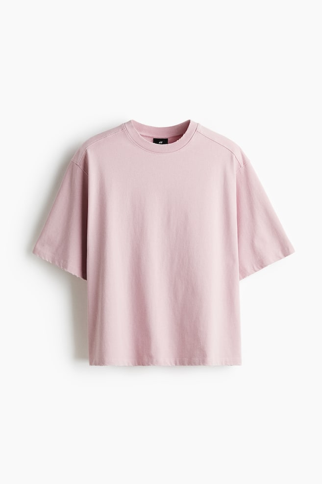 A pink, front-facing, relaxed-fit t-shirt is featuring a ribbed round neck, dropped shoulders, and short sleeves with raw-cut edges. The t-shirt is also displaying a raw-cut hem. - 1