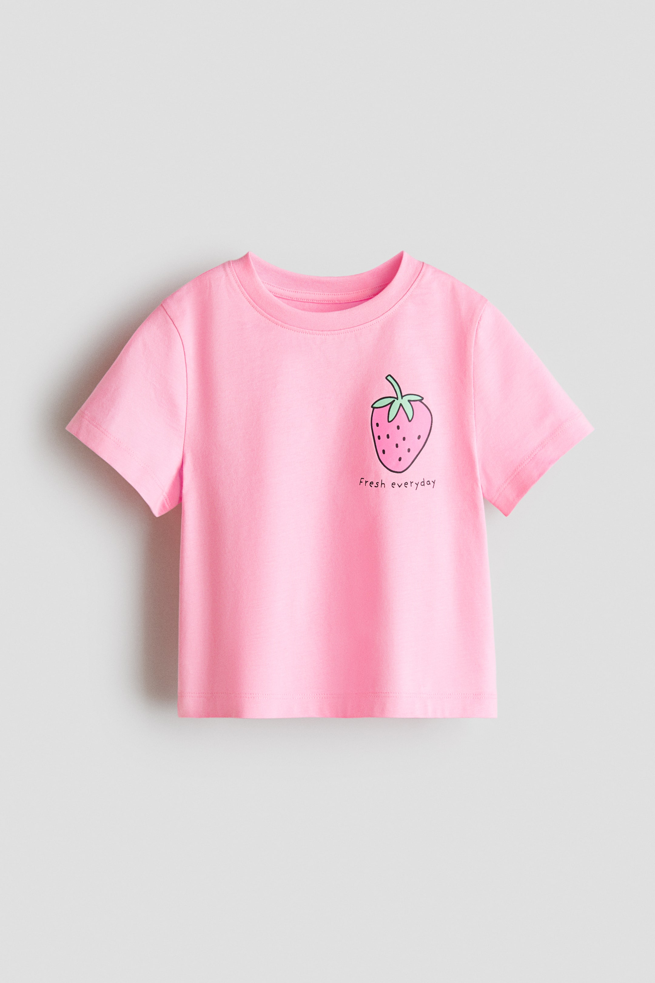 View larger image: A pink t-shirt showcases its front, crafted from soft cotton jersey. It features a ribbed trim around the neckline and a graphic print of a strawberry with the text 'Fresh everyday' beneath it.