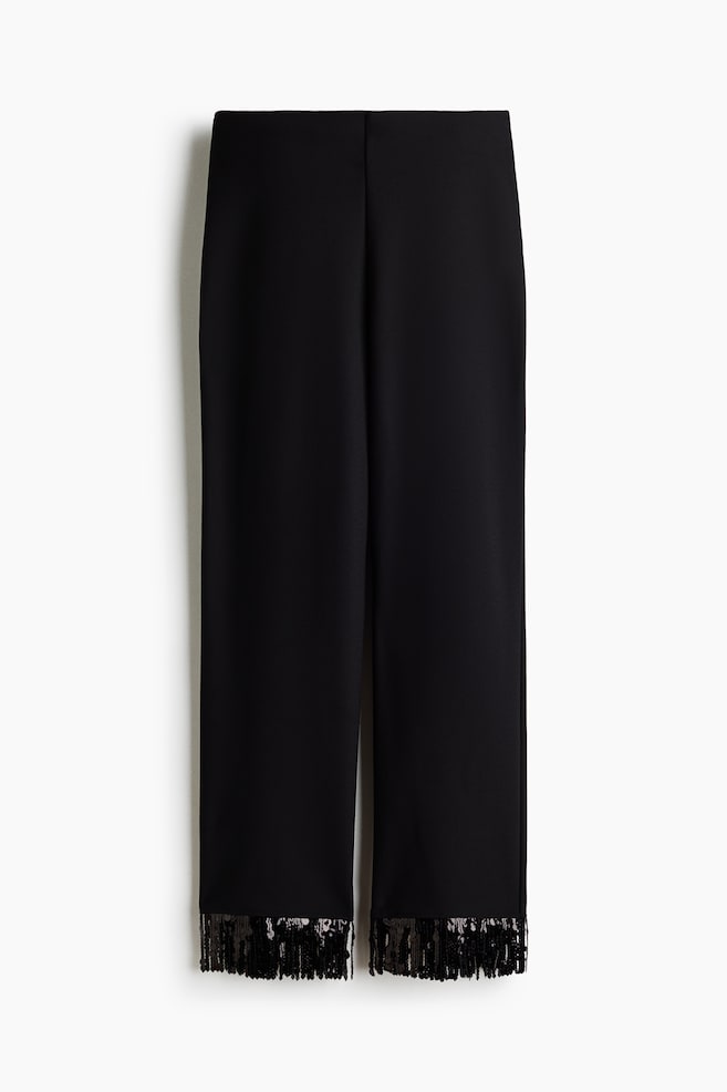 These black wide-leg trousers are hanging facing forwards, showcasing a clean, high-waisted design with straight legs. The hems are finished with a decorative trim of dense, dangling black sequined fringe. - 1