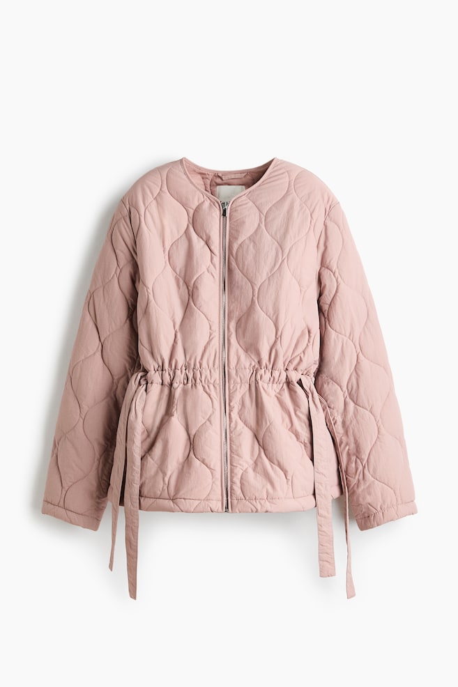A pink quilted jacket is presenting FRONT, featuring a wavy quilting pattern throughout and a collarless, rounded neckline. A silver zipper is running down the center front, and an adjustable drawstring with ties is cinching the waist. - 1