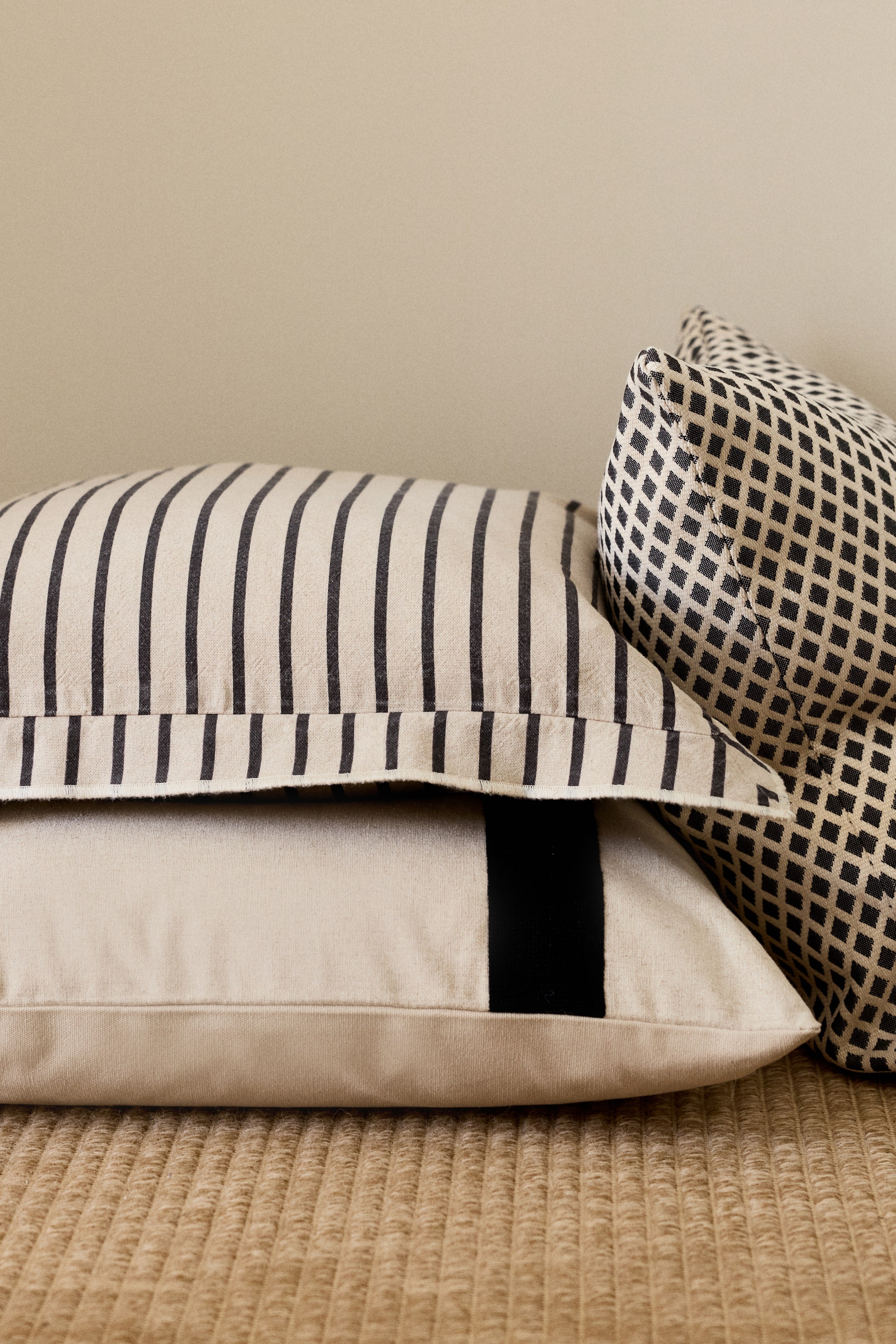 View larger image: The cushion cover showcases its front, adorned with slender black vertical stripes on a light beige woven fabric, complemented by a broad, plain border along its visible edges.