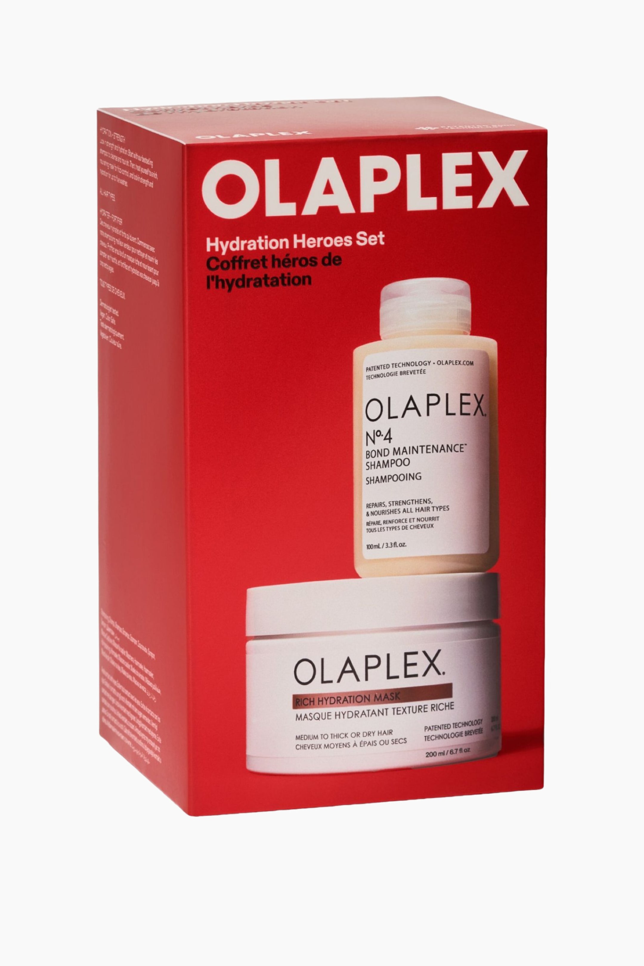 Vis større bilde: Olaplex Hydration Heroes Set står i en vinkel på trekvart, og viser en ярк rød rektangulær eske med tydelig hvit branding. Forsiden av emballasjen viser illustrasjoner av flasken til Olaplex No. 4 Bond Maintenance Shampoo og krukken til Rich Hydration Mask. Venstre sidepanel viser tilleggsinformasjon om produktet og bruksanvisning trykt i hvit tekst.