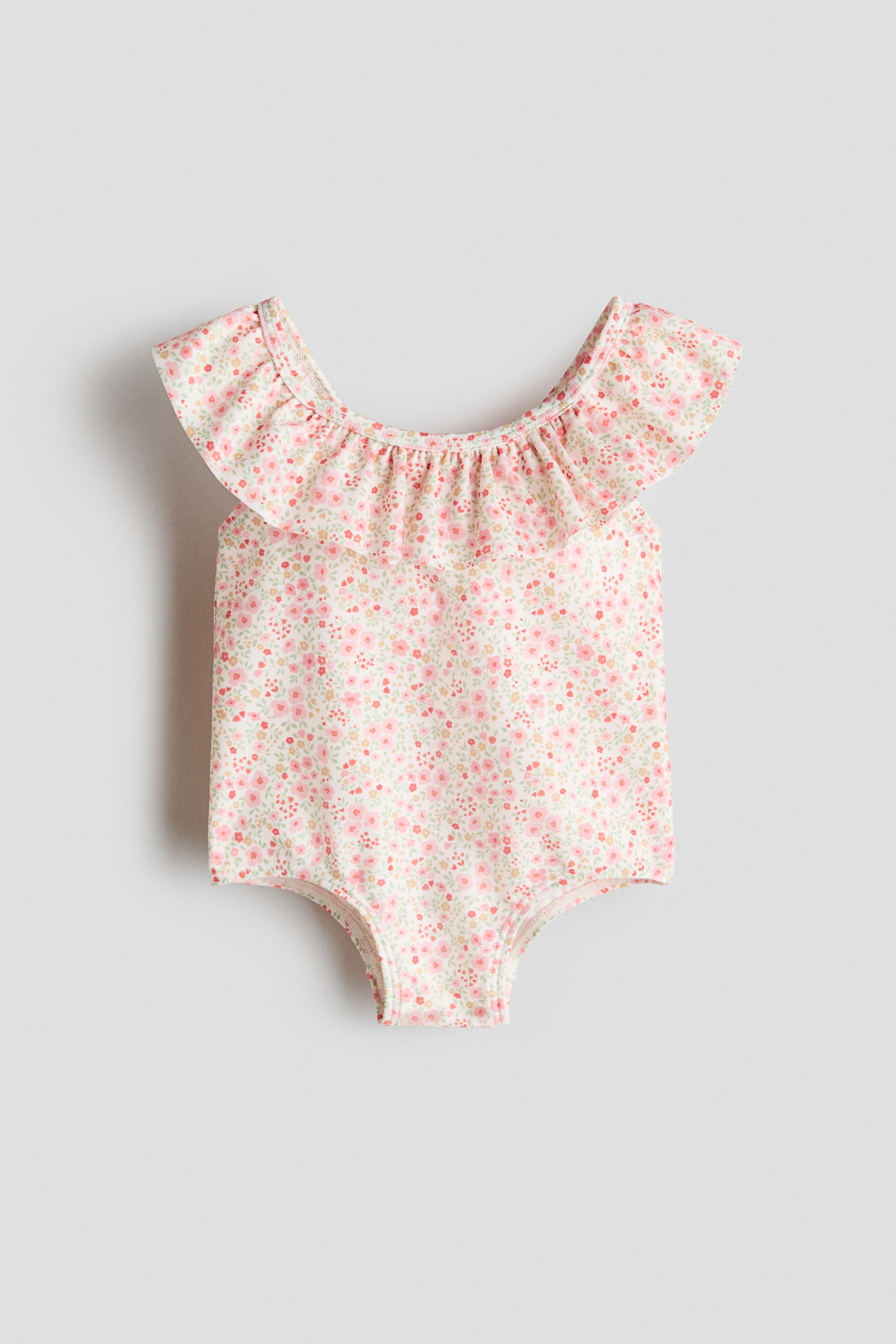 Agrandir l'image: Un maillot de bain présenté de face (FRONT), doté d’un petit imprimé floral rose, vert et jaune sur fond crème. Il est conçu avec un volant froncé autour de l’encolure qui se prolonge sur les épaules.