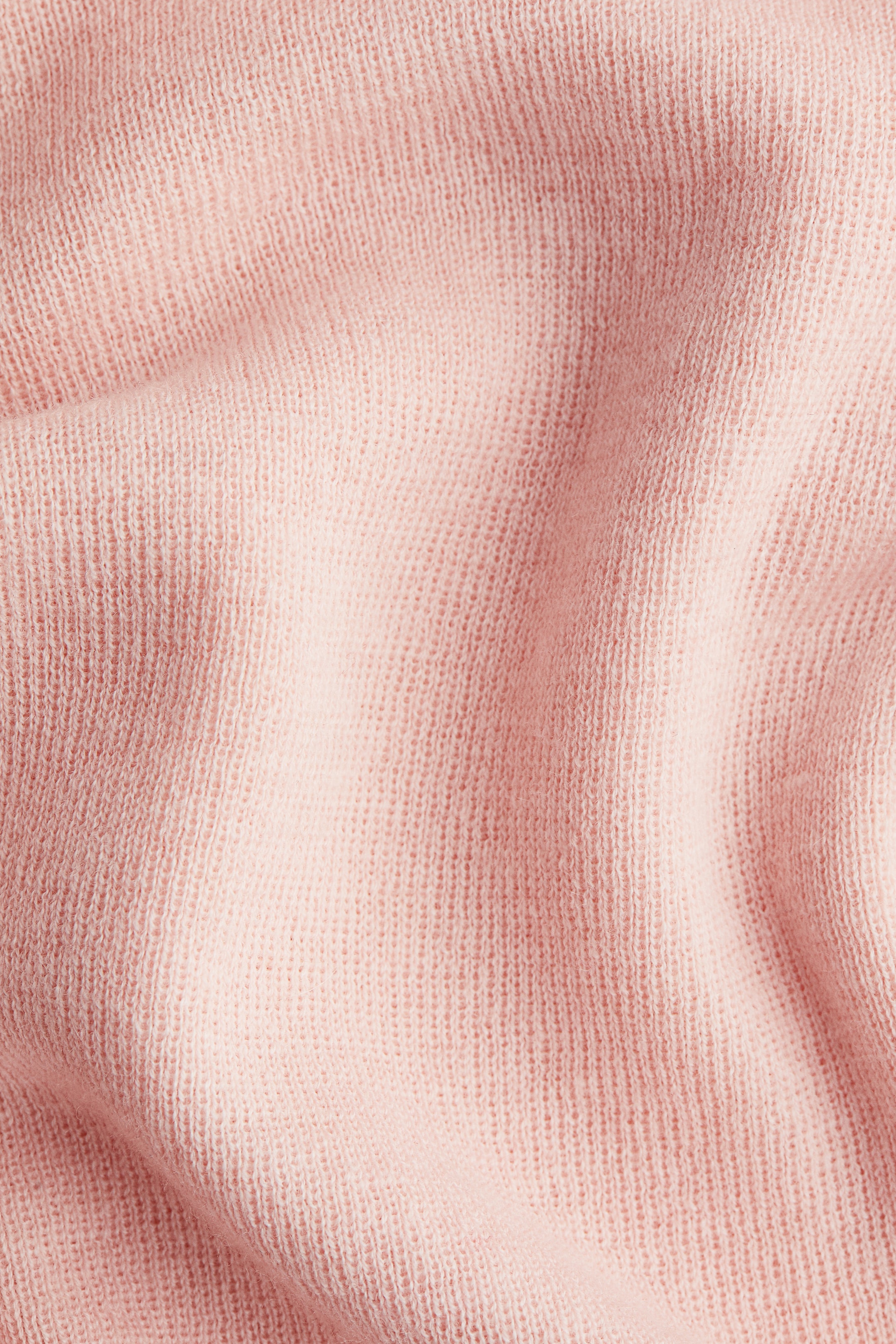 Agrandir l'image: Un tissu en maille fine de couleur rose clair est présenté en gros plan, montrant sa texture douce avec de subtiles lignes de tricot verticales et de légers plis.