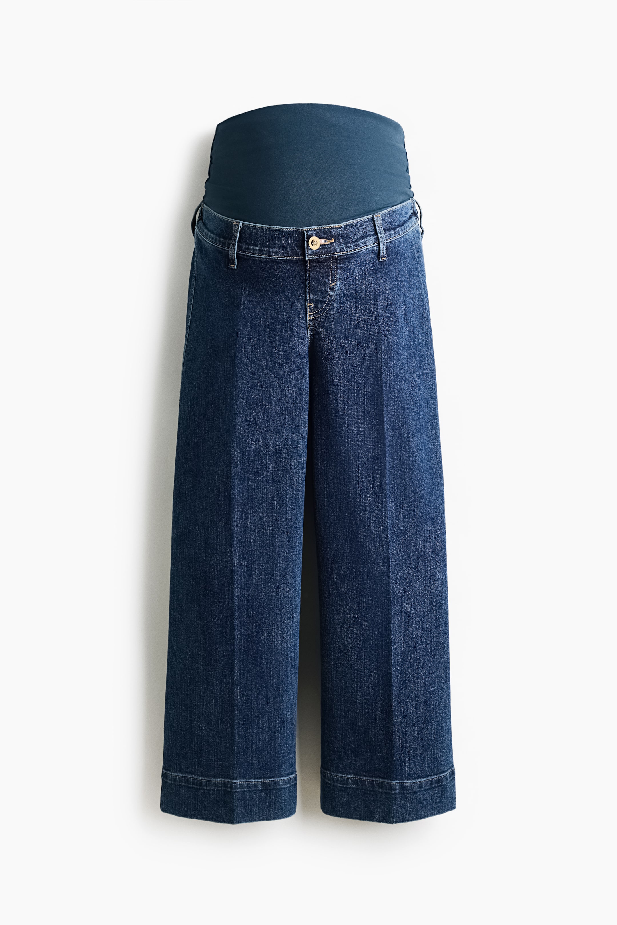 View larger image: Maternity jeans are showcased from the front, featuring a dark blue wash and a wide-leg, cropped silhouette with folded cuffs. They incorporate a dark teal over-the-bump elastic panel at the waist, complemented by a traditional jean waistband, belt loops, and a single gold-toned button and zipper closure below.