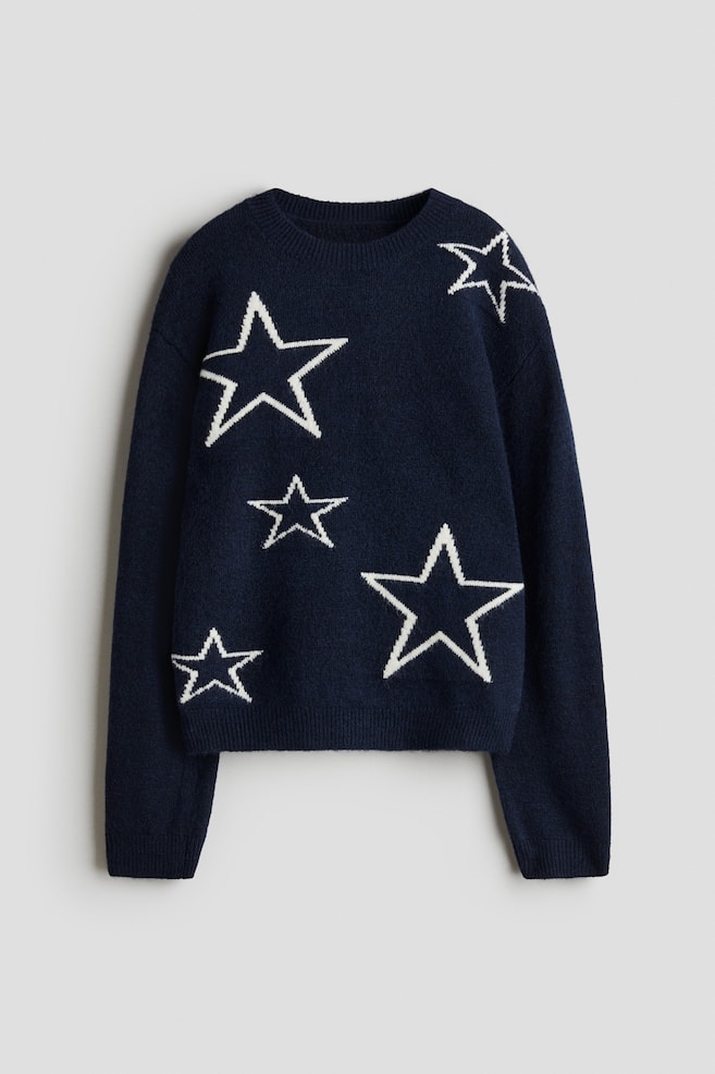 Un pull en maille bleu marine, à coupe ample, est présenté de face, affichant un motif d'étoiles blanches de différentes tailles. Ce pull en maille douce présente un col rond avec bordure côtelée, des épaules tombantes, et des poignets et un ourlet côtelés. - 1