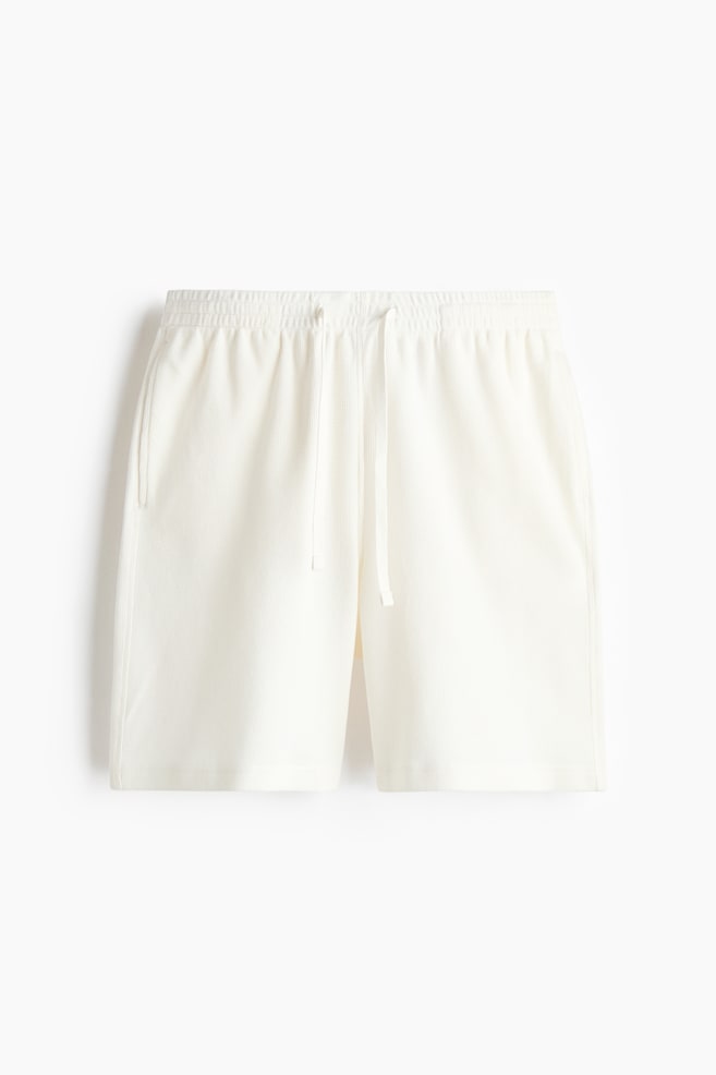 "Off-White Cord-Shorts in Vorderansicht, mit elastischem Bund und Kordelzug. Vertikale Schlitztaschen sind auf beiden Seiten sichtbar." - 1