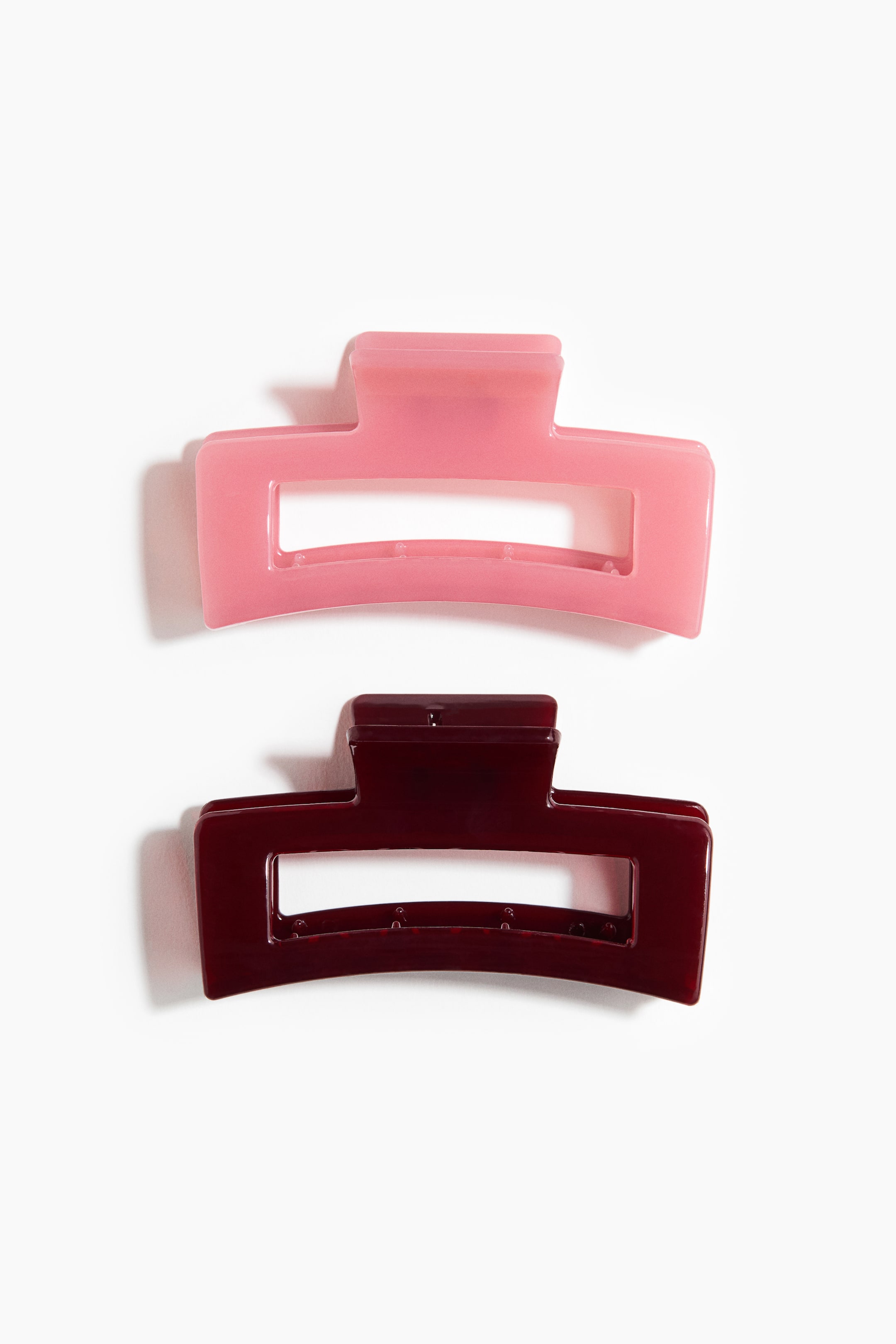 View larger image: Two 8.5 cm plastic hair claws are shown from the front. The top claw is translucent pink and the bottom claw is translucent burgundy, both featuring a rectangular design with a curved jaw and visible inner teeth.