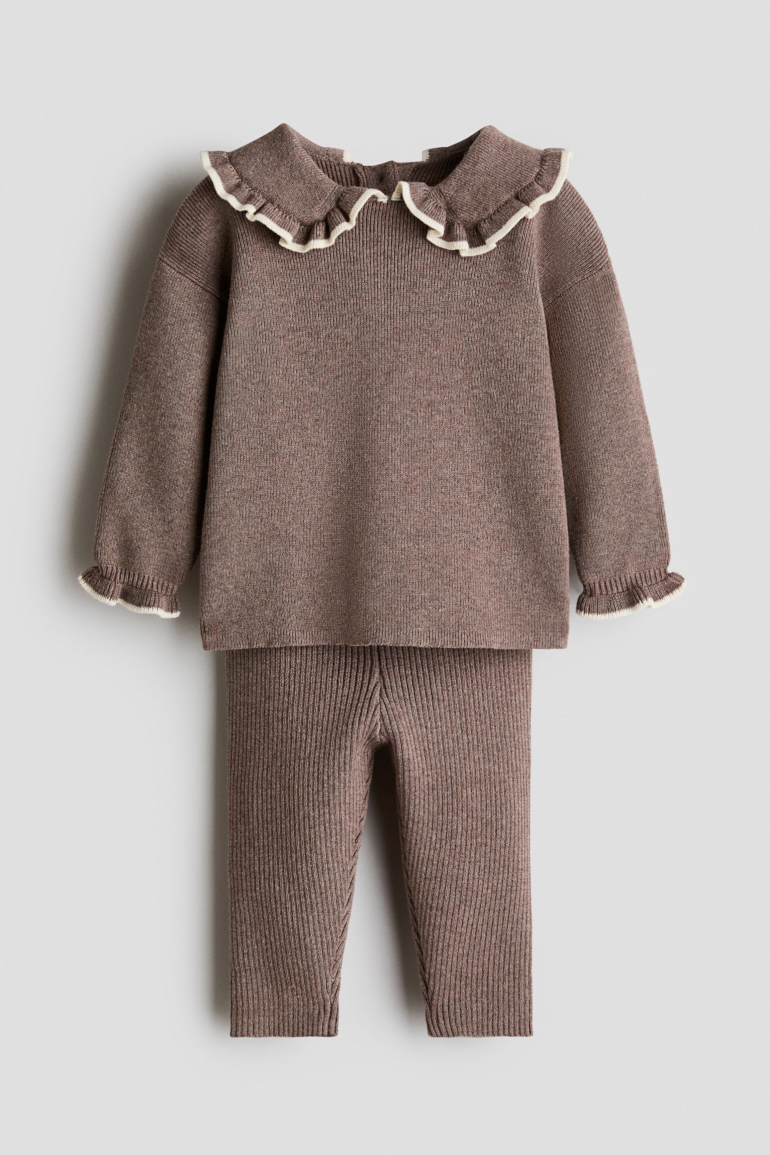 Een tweedelige gebreide set in een stoffige bruin mélange wordt van voren getoond, bestaande uit een trui met lange mouwen en bijpassende leggings. De trui heeft verlaagde schouders, gerimpelde boorden met crèmekleurige afwerking en een brede kraag met een bijpassende crèmekleurige rucherand. - 1
