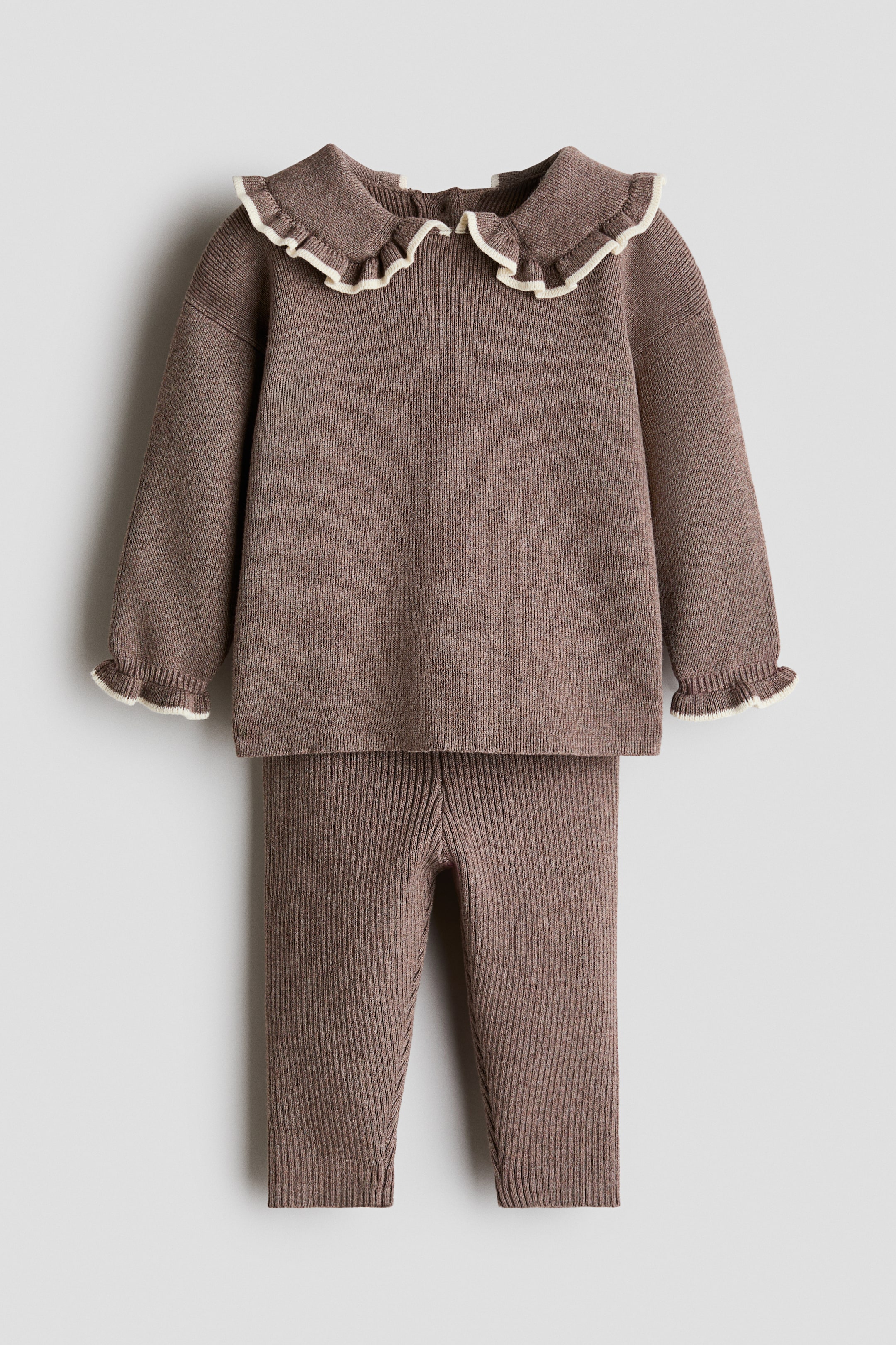 Größeres Bild anzeigen: Ein zweiteiliges Strickset in staubigem Braun-Melange ist von vorne zu sehen und besteht aus einem langärmligen Pullover und einer passenden Leggings. Der Pullover zeigt überschnittene Schultern, gerüschte Bündchen mit cremefarbener Einfassung sowie einen breiten Kragen mit passender cremefarbener Rüschenkante.