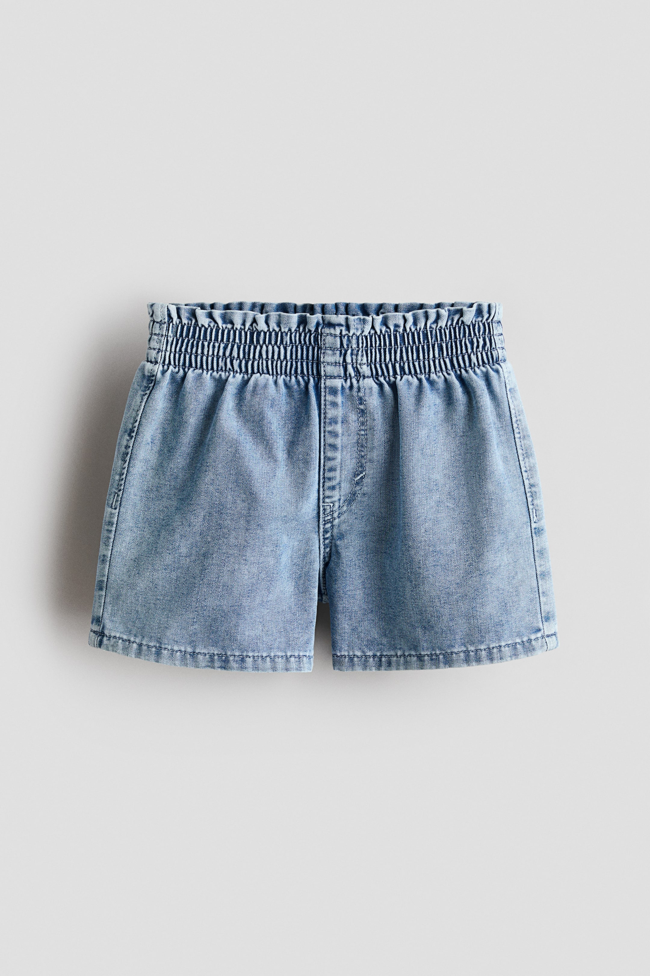 View larger image: Loose-fit shorts in washed lightweight denim are showcased at the front, featuring an easy pull-on waist with smocked elastication and a visible faux fly.