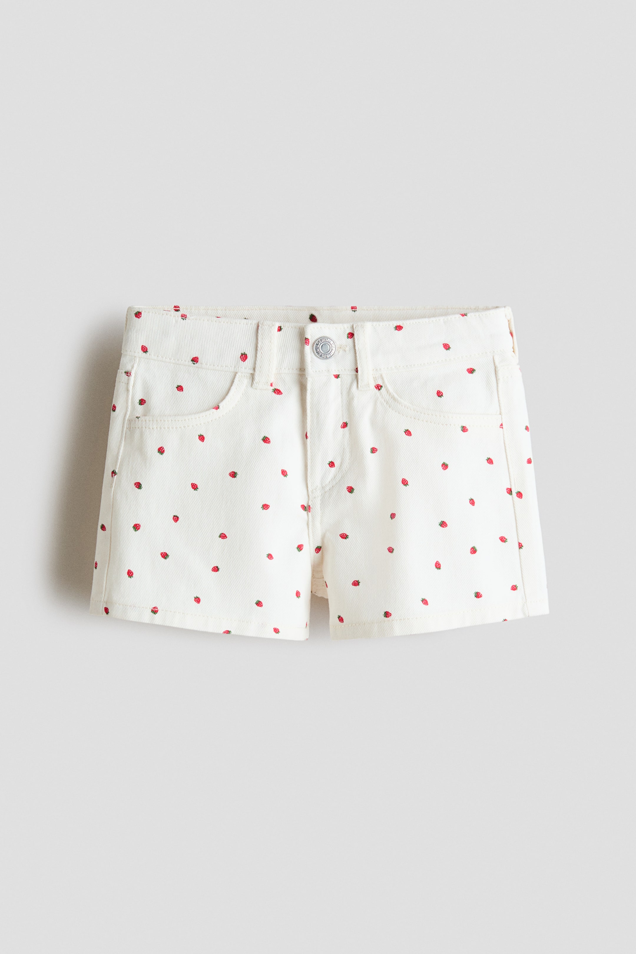 Ingrandisci l'immagine: I pantaloncini di jeans in cotone sono mostrati in vista frontale, con una base di colore bianco e una stampa sparsa di fragole rosse. Sono progettati con una cintura, passanti per cintura, una chiusura con bottone in metallo e due tasche frontali curve.