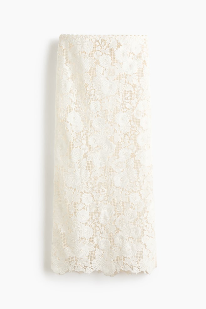 A cream lace skirt featuring a dense floral pattern and an underlying light-coloured lining. The skirt presents a straight silhouette with a scalloped hemline. - 1