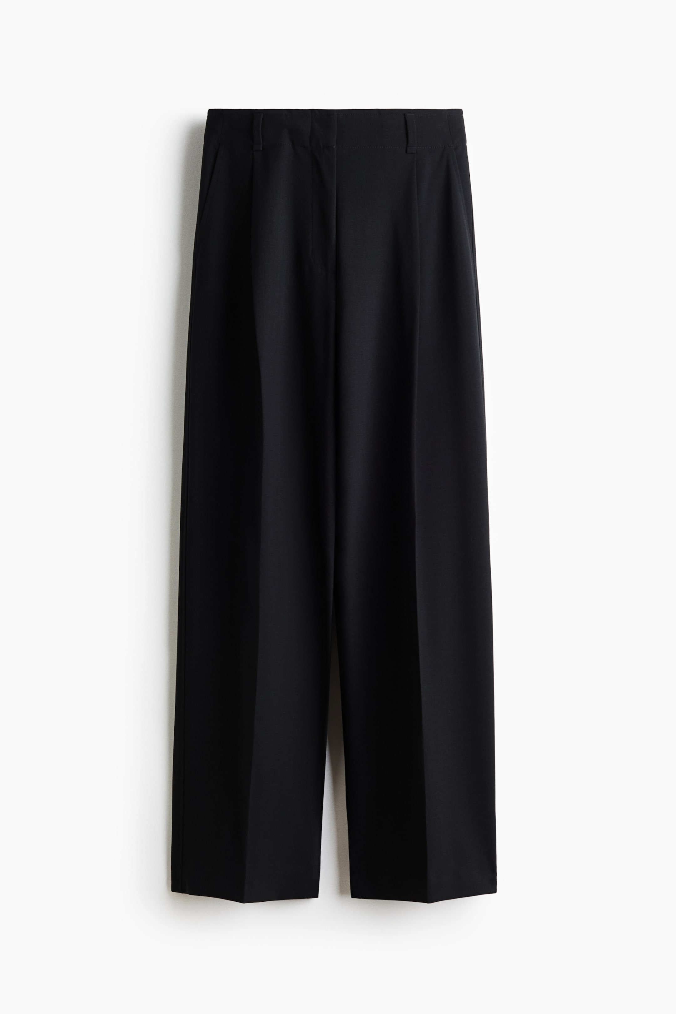 Ver imagen más grande: Unos pantalones negros se muestran de frente, con una cinturilla plana, trabillas visibles para el cinturón y pinzas. Los pantalones presentan perneras anchas y rectas con marcadas dobleces centrales.