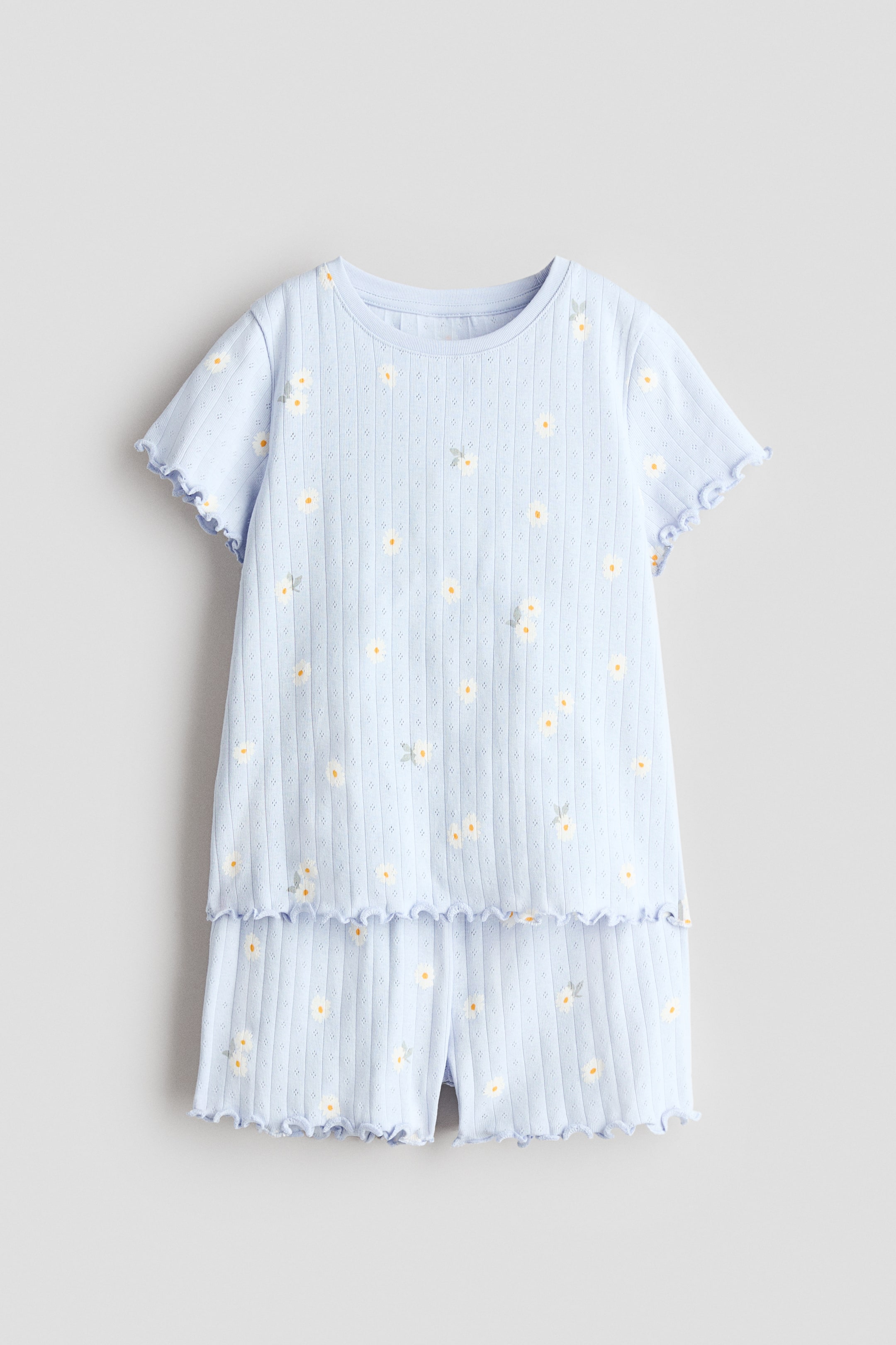 View larger image: FRONT: Light blue pointelle jersey pyjamas feature a short-sleeved top and shorts, both adorned with a scattered print of small white and yellow flowers. The top has a round neckline and ruffled overlocked trims on its sleeves and bottom hem, while the matching shorts boast an elasticated waist and ruffled overlocked leg openings.