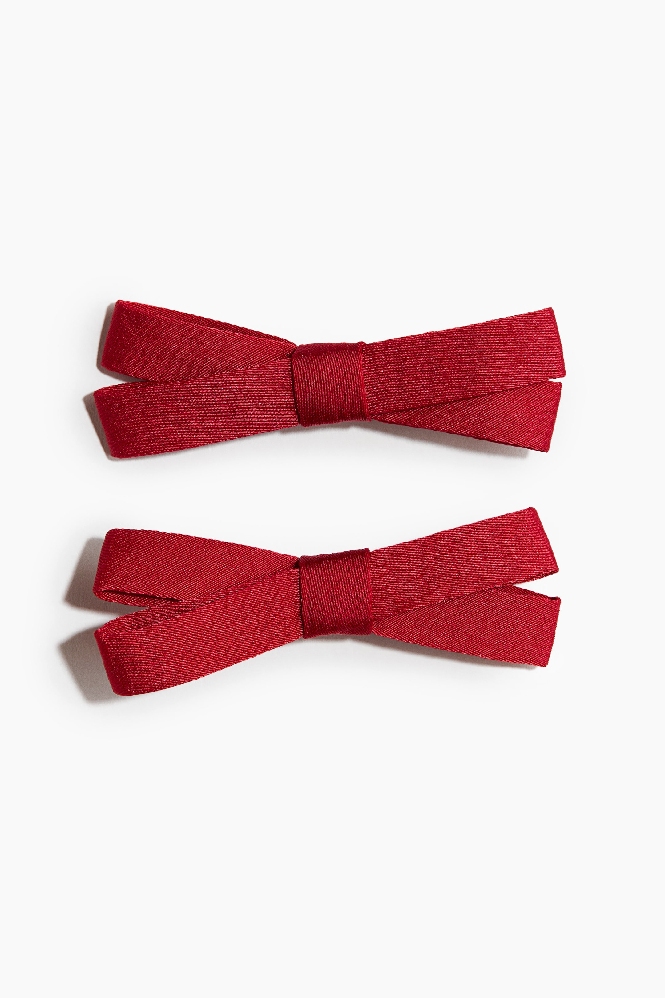 View larger image: Two metal hair clips decorated with narrow red fabric bows are facing forwards, stacked vertically. Each clip features a flat, structured bow crafted from finely textured red ribbon with a matching wrapped centre.