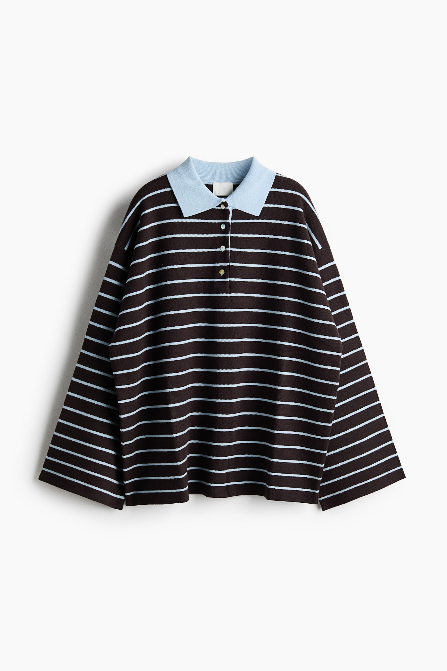 Oversized poloshirt is van voren te zien, met een donkerbruine gebreide body met dunne, horizontale lichtblauwe strepen en een contrasterende lichtblauwe kraag. Het shirt heeft een knoopsluiting met vier knopen, verlaagde schouders en wijde, lange mouwen met open manchetten.