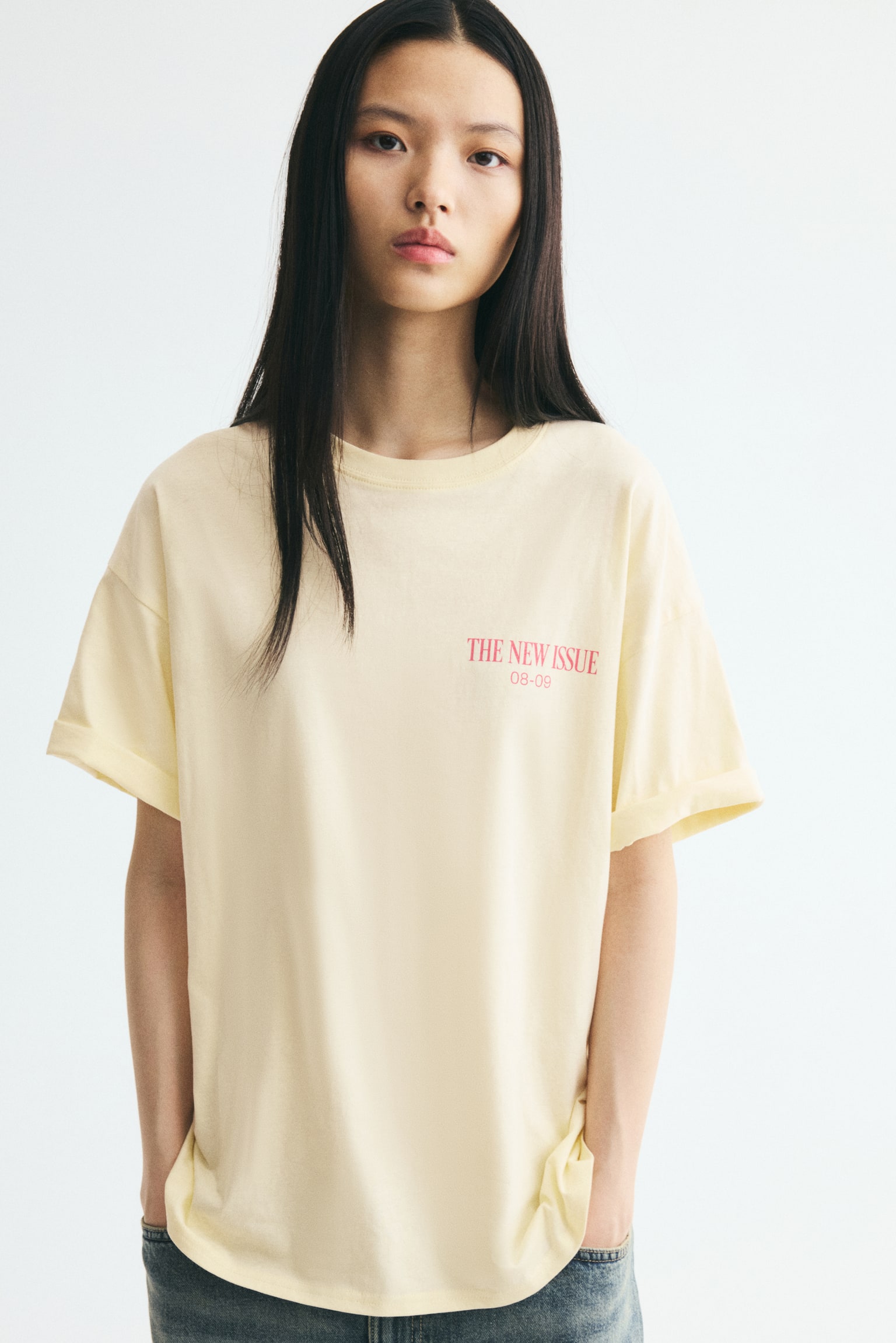 A light yellow oversized t-shirt in cotton jersey is displaying its front, featuring a small pink text print reading 'THE NEW ISSUE 08-09' on the chest, a ribbed trim around the neckline, dropped shoulders, and a straight-cut hem. - 1