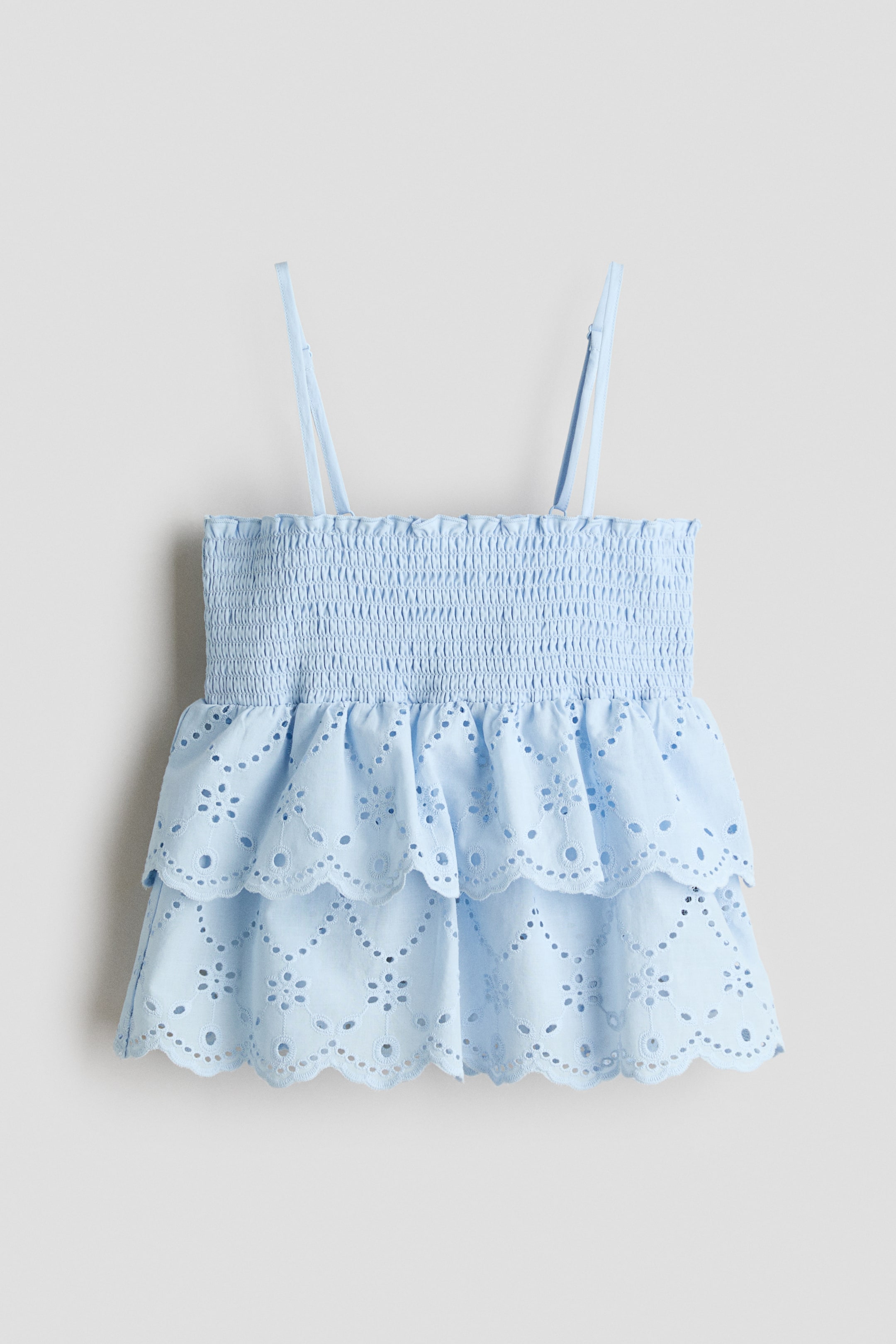 View larger image: A light blue top, crafted from a cotton weave, is displayed from the front, featuring a straight neckline and slim shoulder straps. The top highlights smocking at the top and a double-layered, scalloped peplum with broderie anglaise detailing.