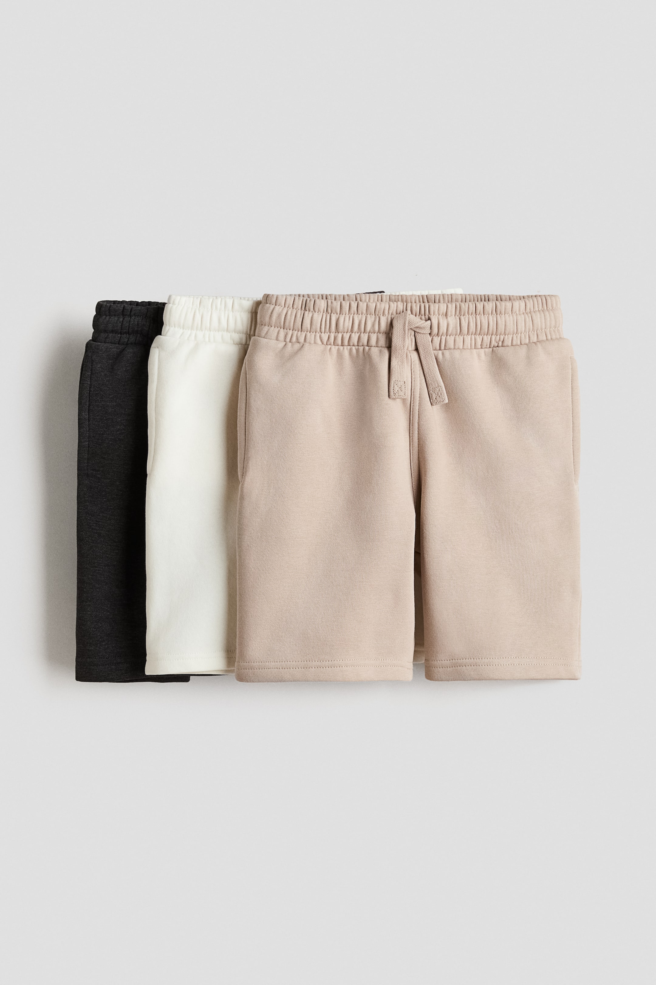 View larger image: Three pairs of shorts crafted from lightweight sweatshirt fabric are displayed facing FRONT, showcasing an elasticated, drawstring waist along with discreet side pockets. Available in black, white, and beige.