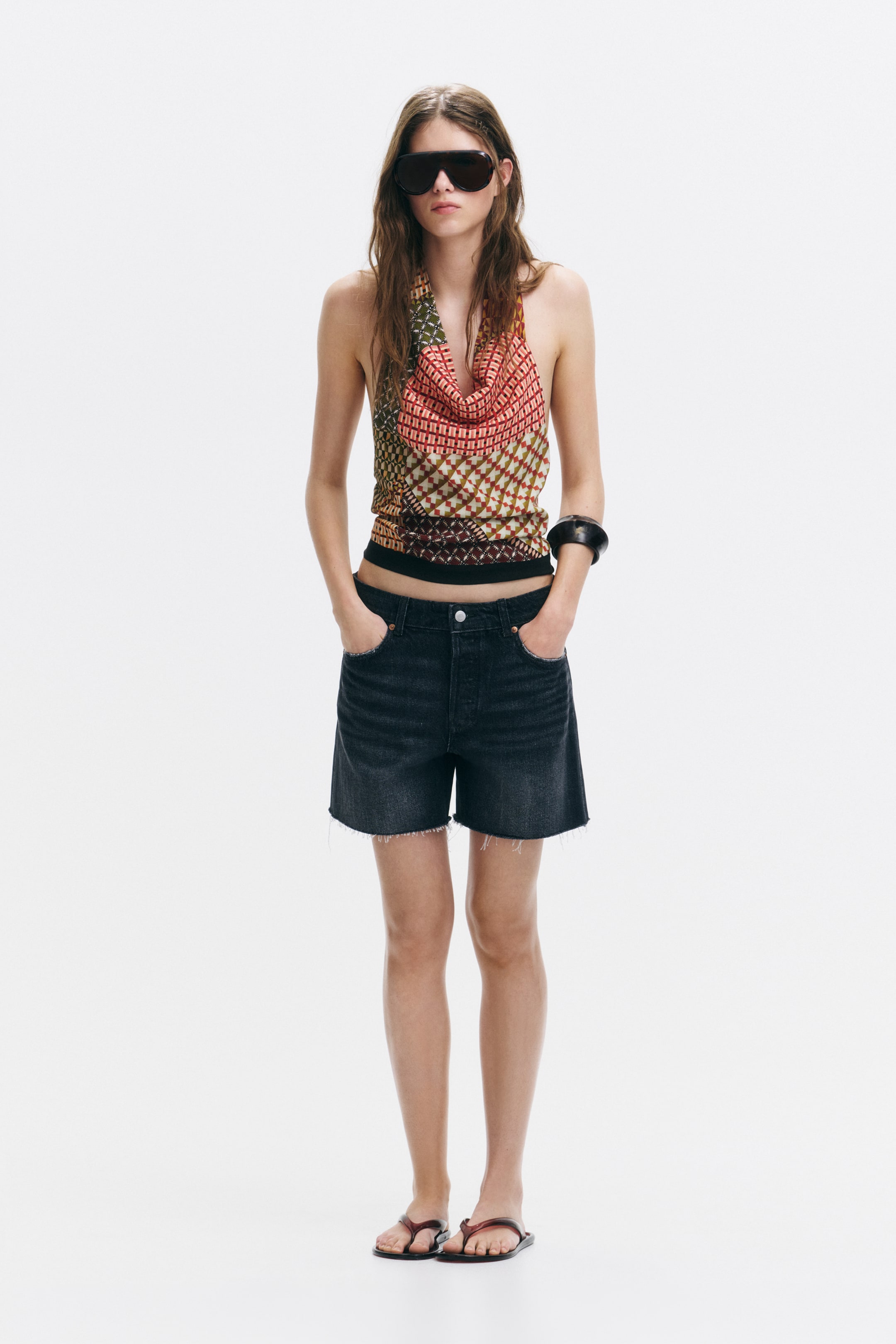 View larger image: The model is wearing rigid cotton denim 5-pocket shorts, showcasing worn details, a visible button fly, and raw-edge hems. The model stands with hands in the front pockets of the shorts.