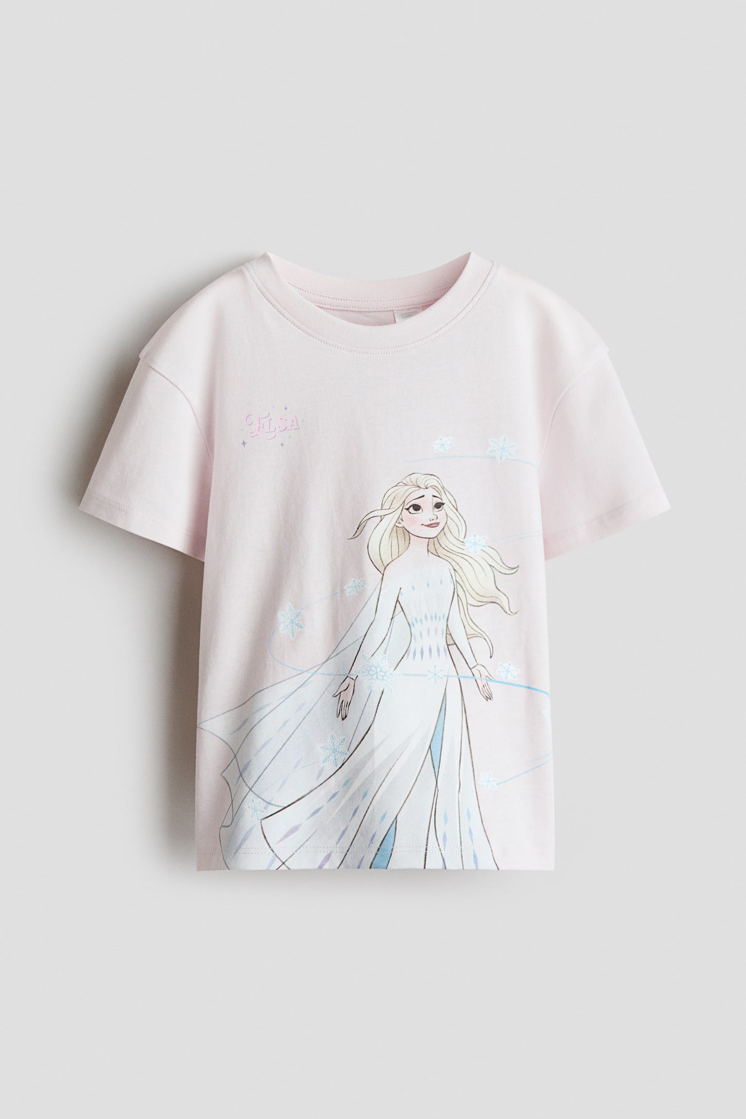 A pink t-shirt is featuring a ribbed crew neck and short sleeves. Its front is displaying a graphic print of a blonde character in a white dress, surrounded by blue snowflakes and the stylized word "Elsa." - 1