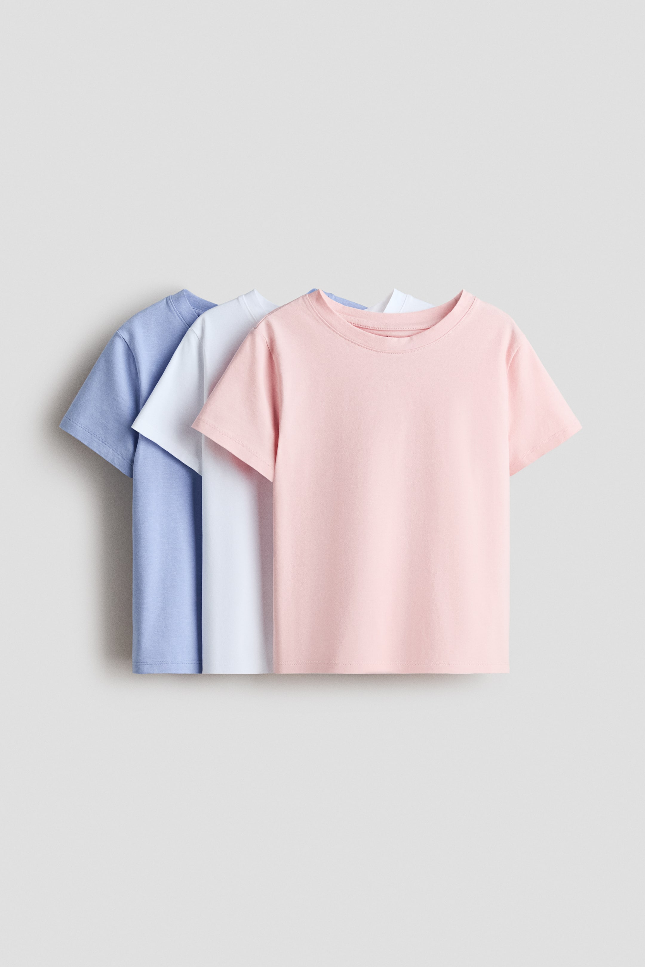 View larger image: Tops in soft cotton jersey with a round neckline and short sleeves are displaying in pink, white, and light blue, presented front-facing in a layered arrangement.