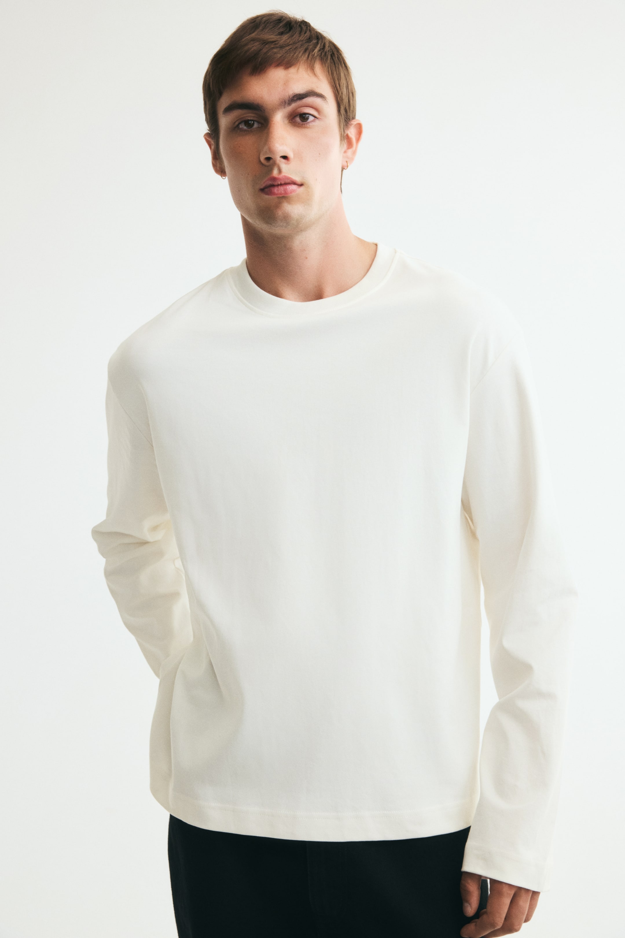 View larger image: A long-sleeve tee in off-white interlock jersey is being worn by the model, paired with black trousers. The relaxed-fit tee features a rib-trimmed crew neckline, dropped shoulders, and a straight hem.