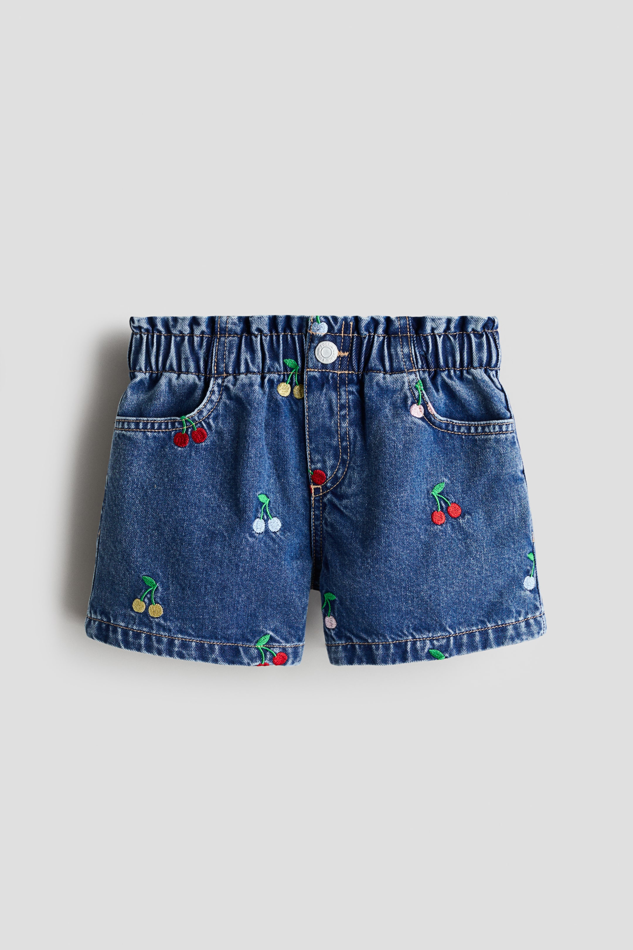 View larger image: The denim shorts are presenting a front view, featuring a blue wash with a shirred waistband, a single button fastening, and two front pockets. Scattered cherry embroideries in various colours are detailing the fabric.