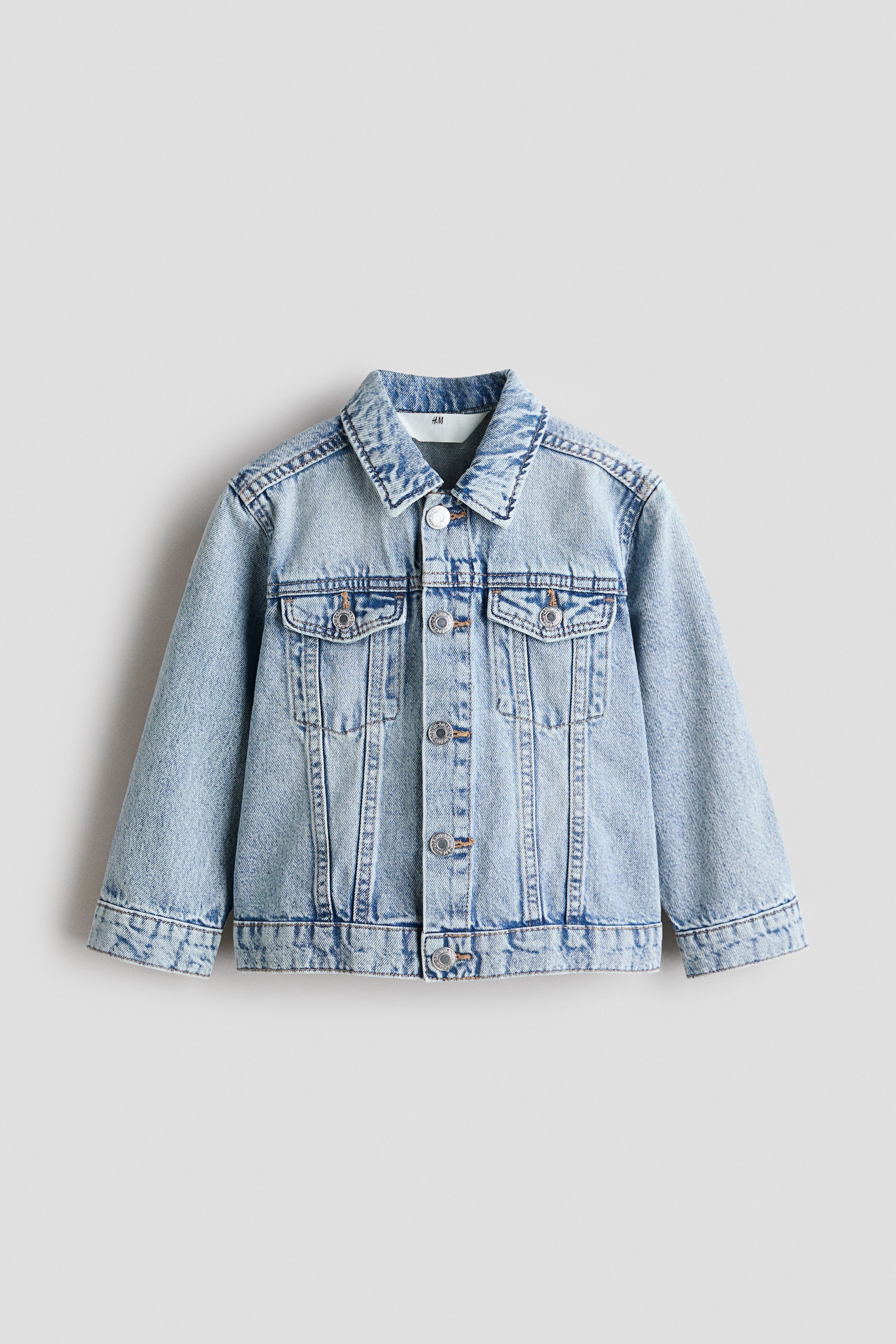 View larger image: A classic light blue denim jacket shown from the front, featuring a turned-down collar, snap buttons down the front and on the cuffs, and two chest pockets with flaps and snaps.