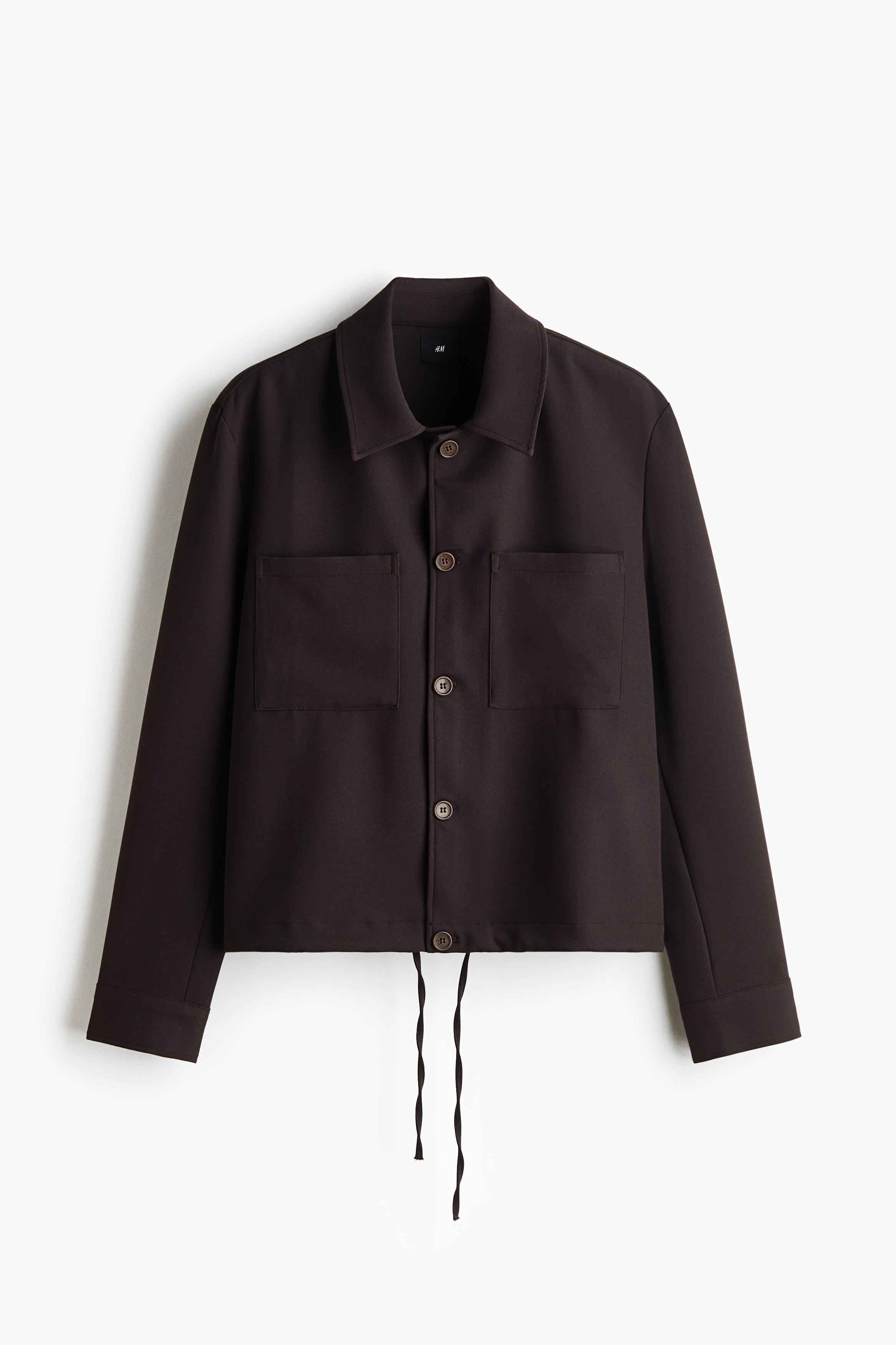 TamnosmeÄa overshirt jakna od mekog tkanja nosi se preko crnog topa s okruglim izrezom i odgovarajuÄih pantalona. Overshirt ima Å¡iljast okovratnik, prednje kopÄanje na dugmad, spuÅ¡tena ramena i dva velika naÅ¡ivena dÅ¾epa na grudima.
